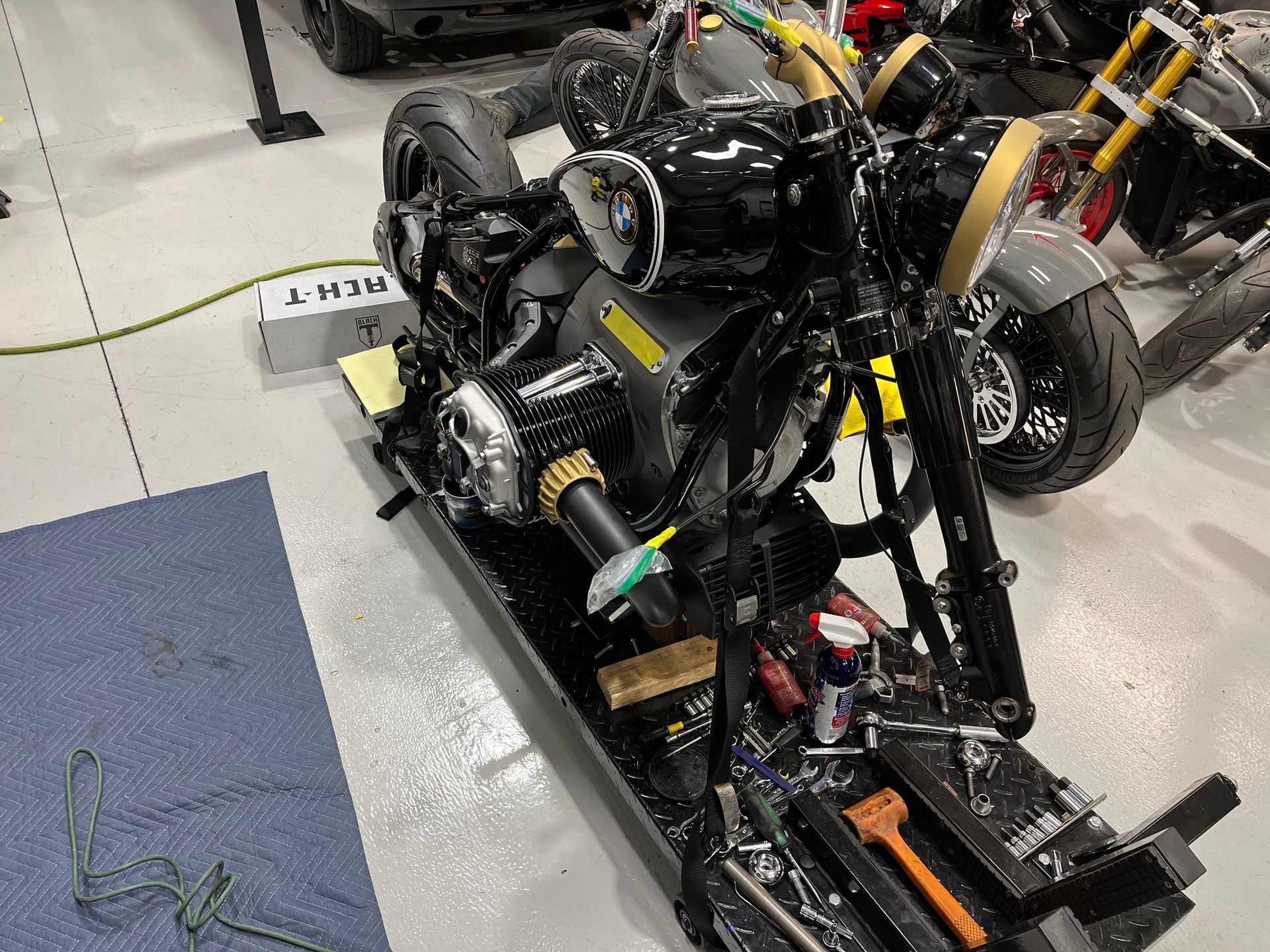 Black vehicle chassis with exposed wheels and wiring on a factory floor, seen from above