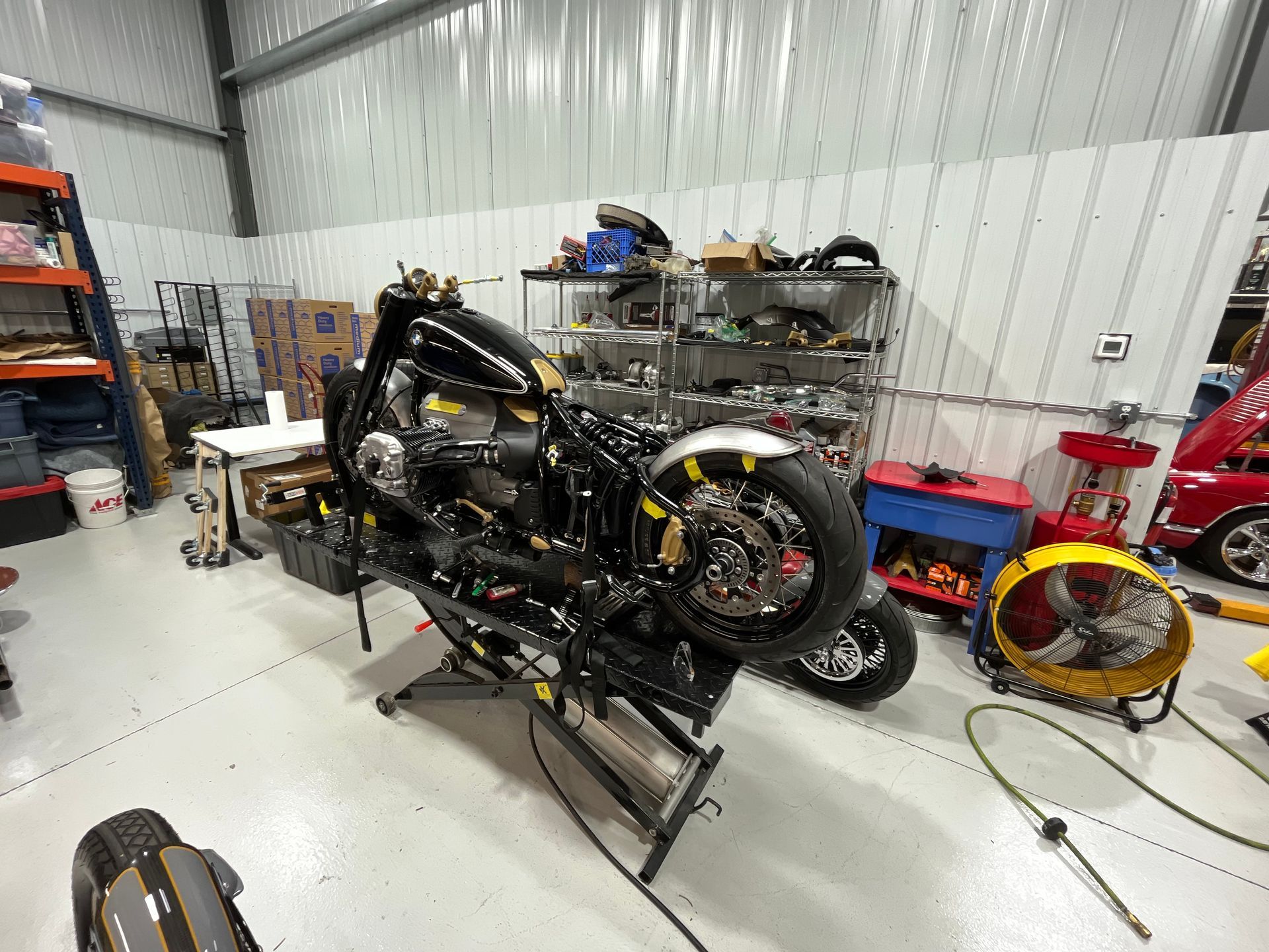 Motorcycle in a workshop, partially disassembled on a stand, with tools and parts scattered nearby.