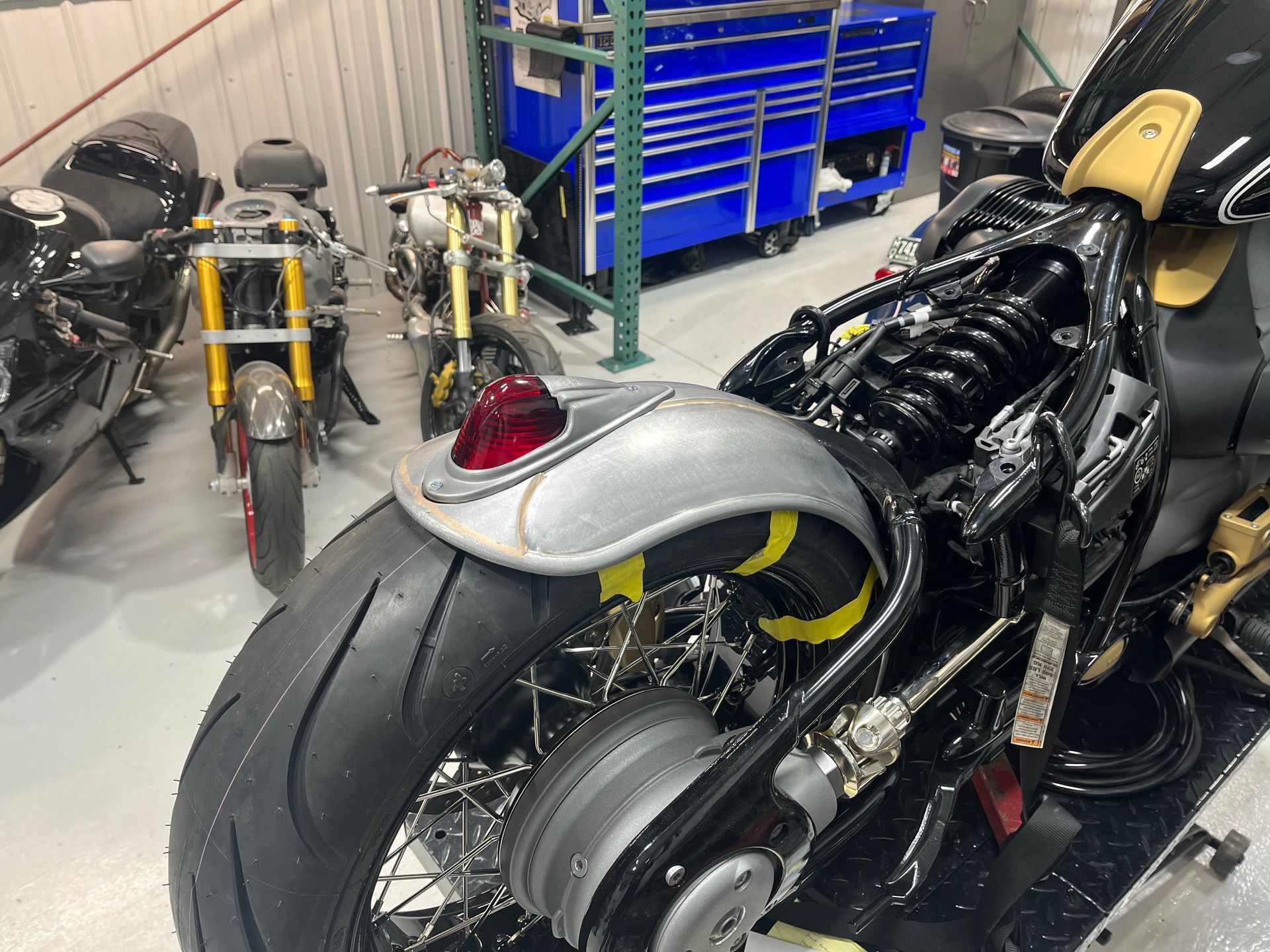 Custom motorcycles parked in a workshop, including a black bike in the foreground and red and blue bikes behind it