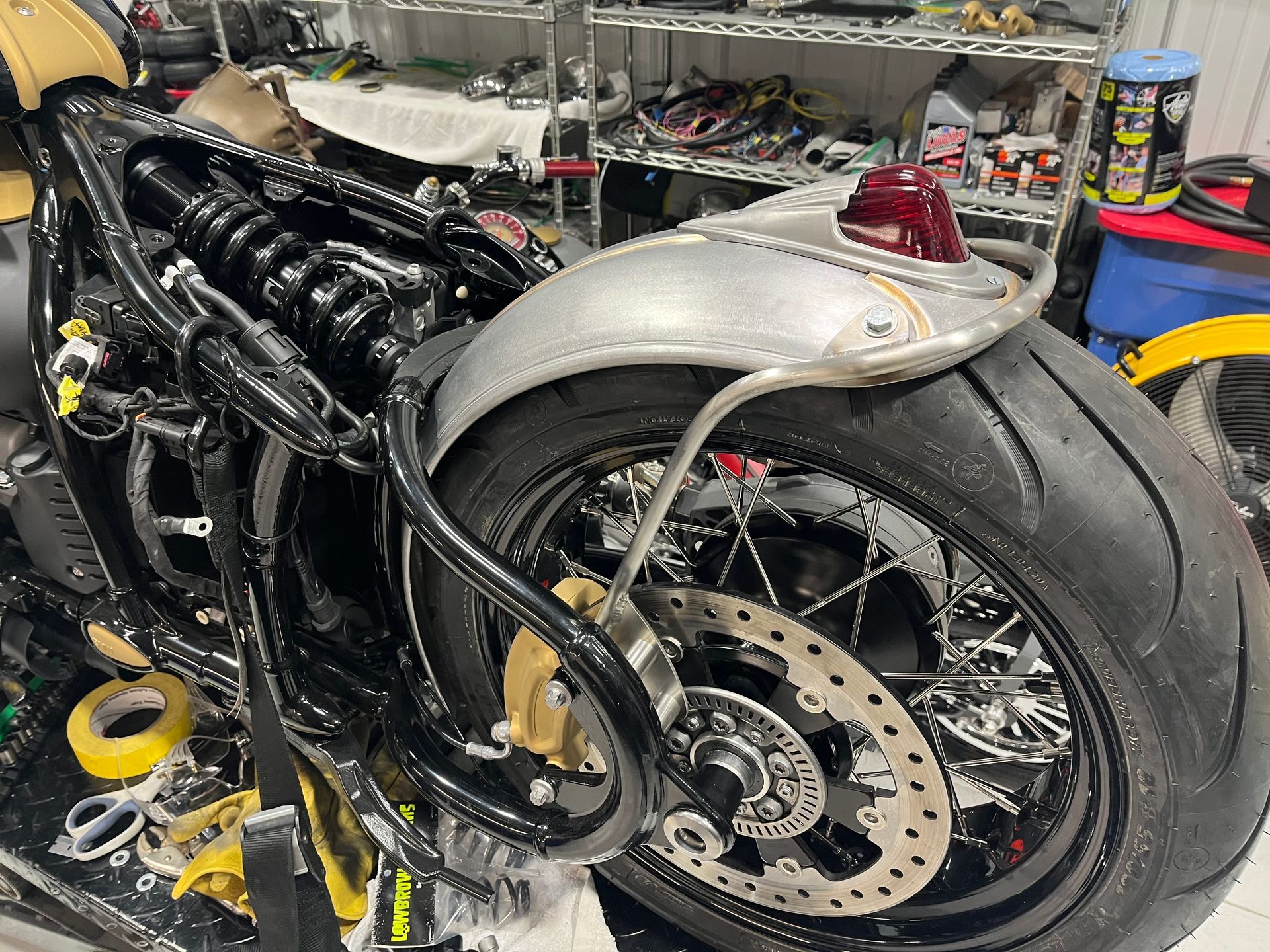 Custom black motorcycle with silver bodywork and exposed rear wheel in a workshop garage