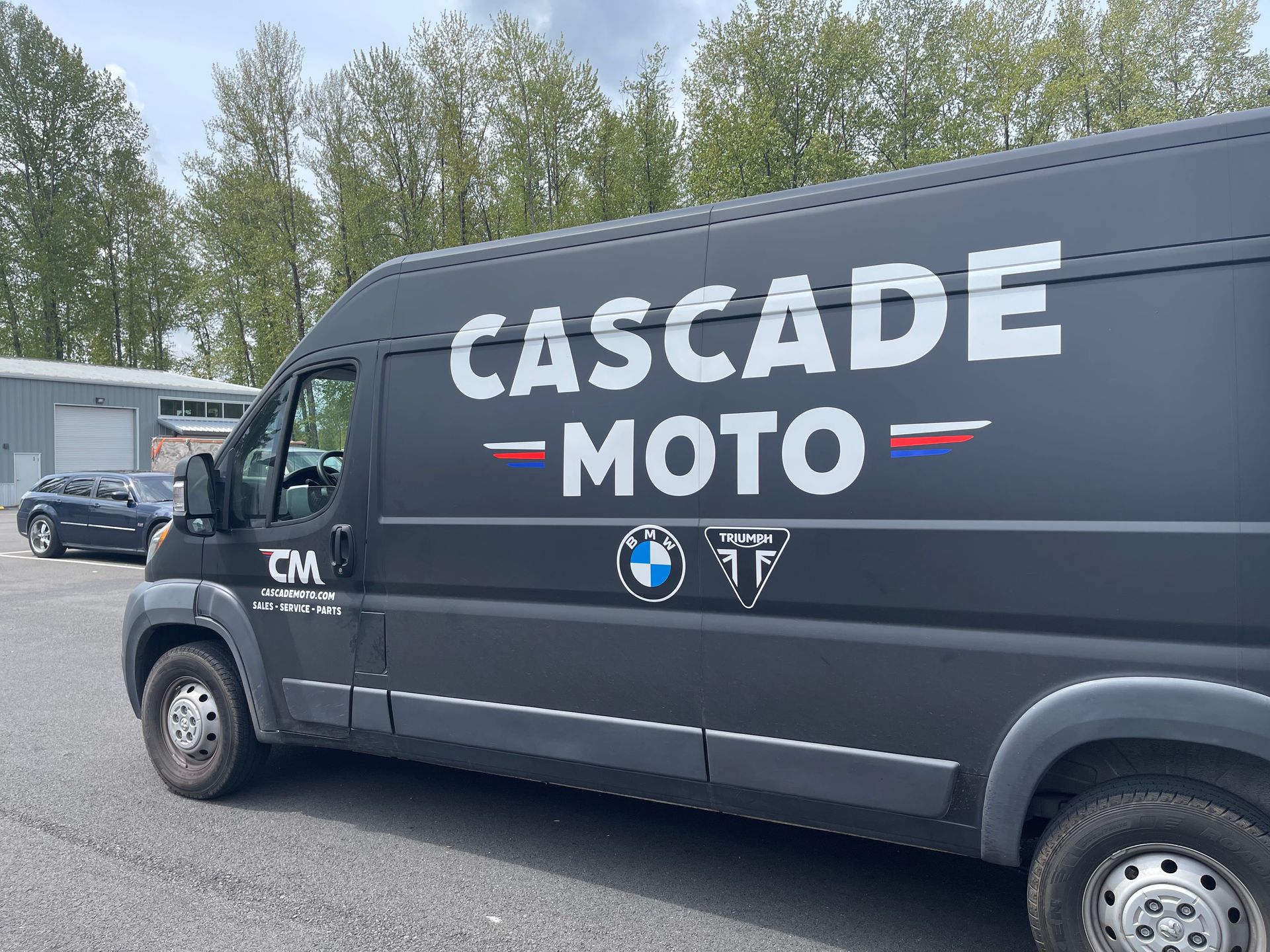 Black Cascade Moto van parked outdoors with trees in the background
