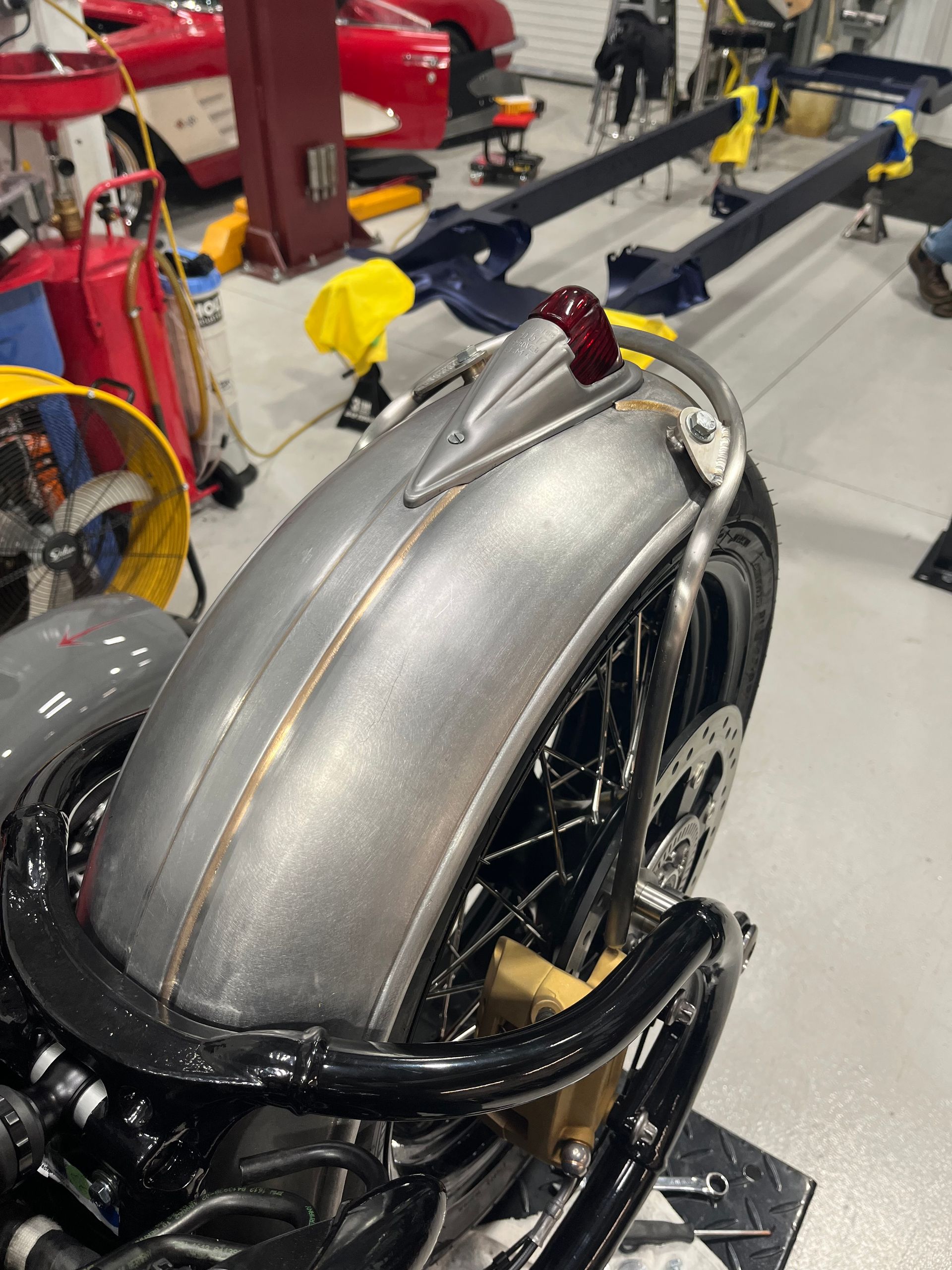Silver motorcycle with a clear windshield and black frame in a workshop, surrounded by tools and equipment