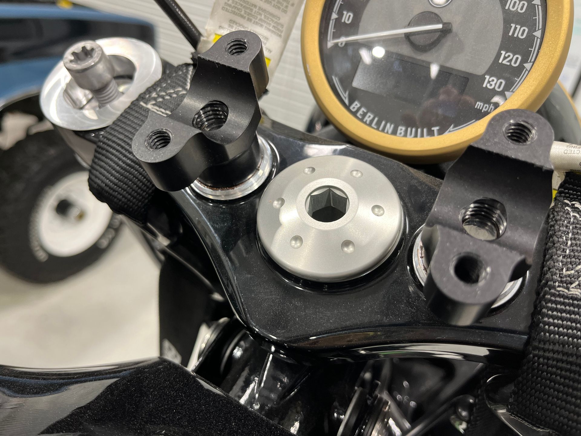 Close-up of a motorcycle handlebar with a speedometer, silver mount, and black controls