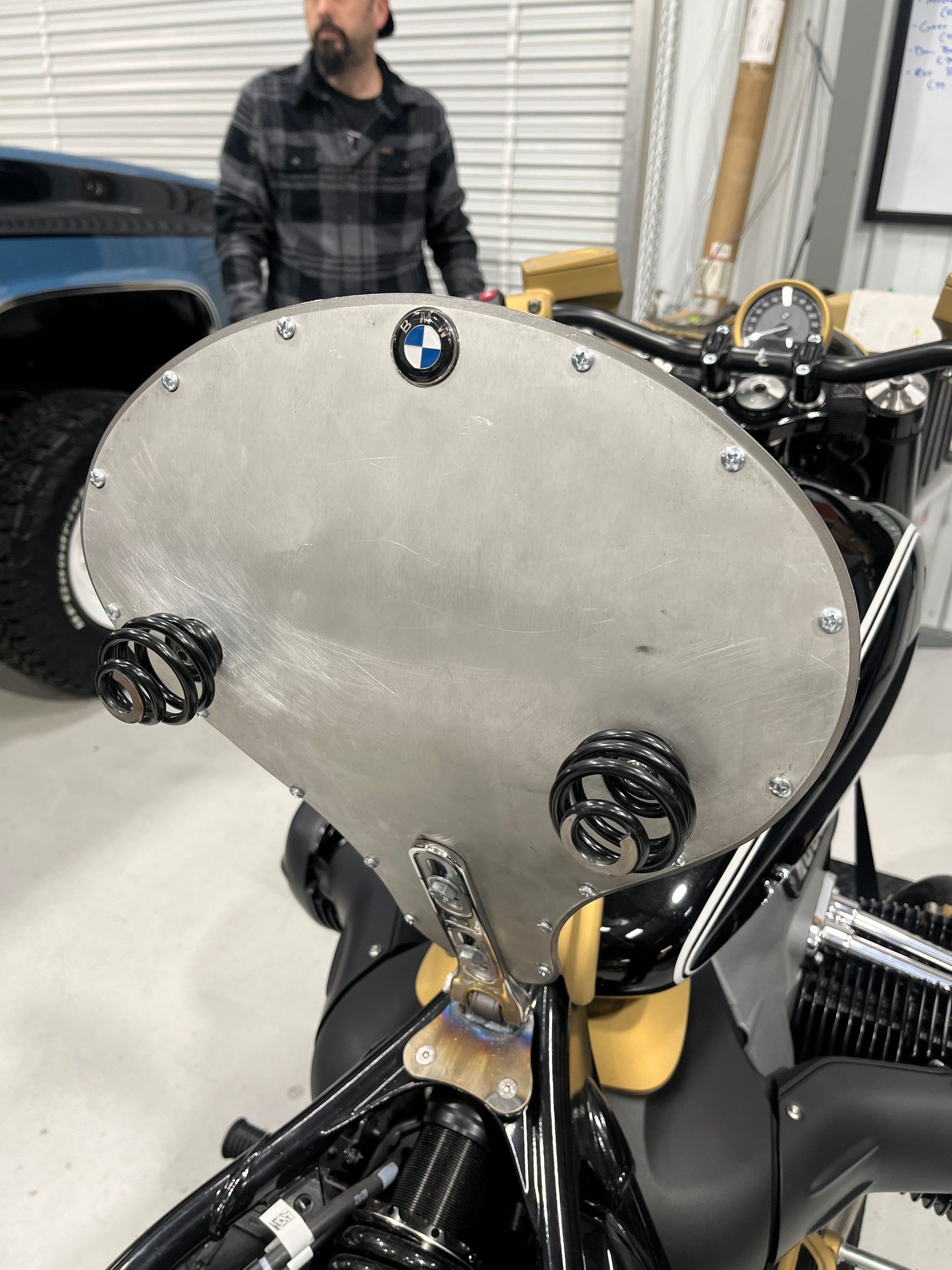 BMW motorcycle with a large silver windshield in a workshop, with a man standing in the background