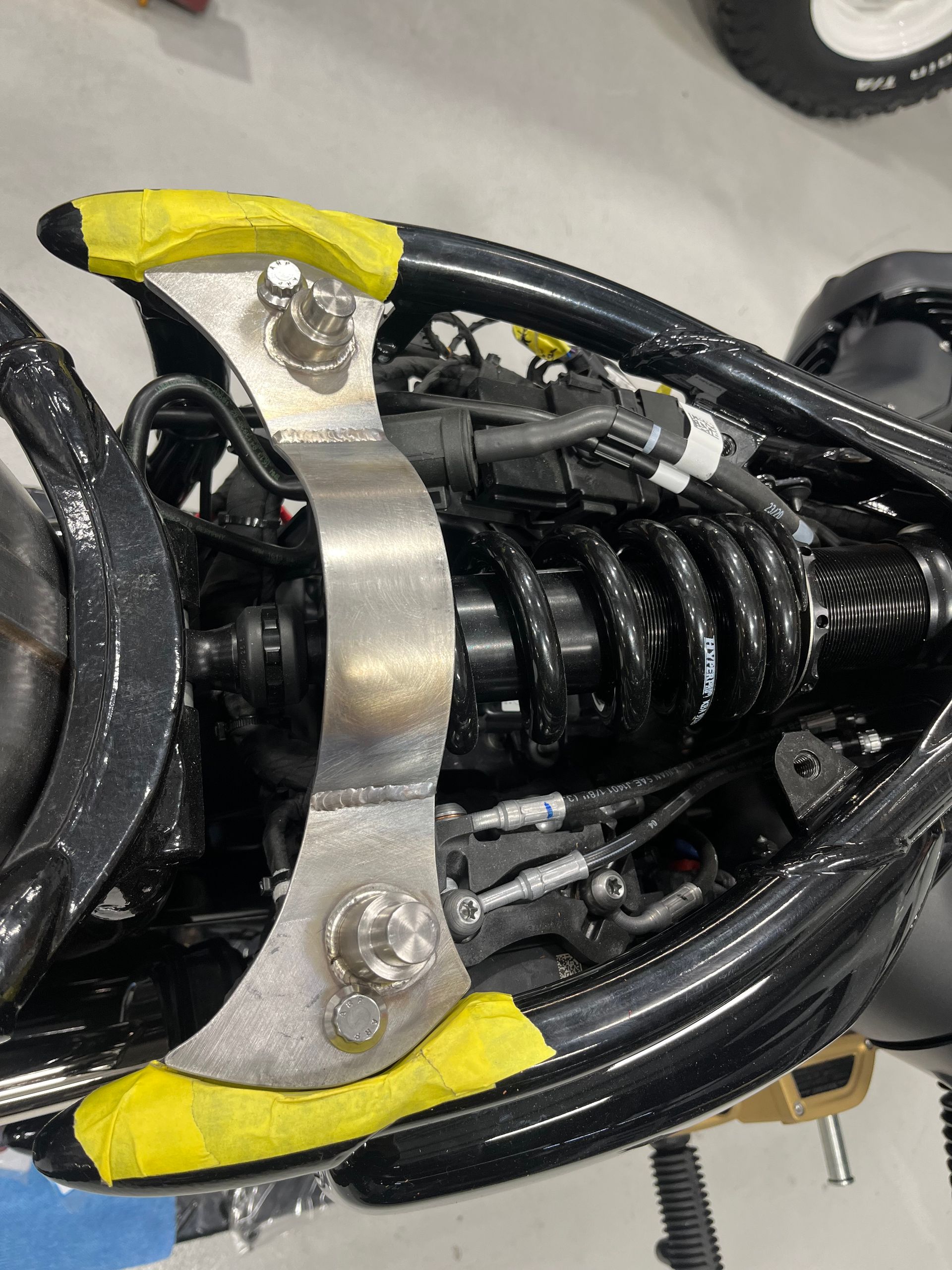 Close-up of black coiled tubing secured by a metal bracket with yellow tape on a mechanical assembly.