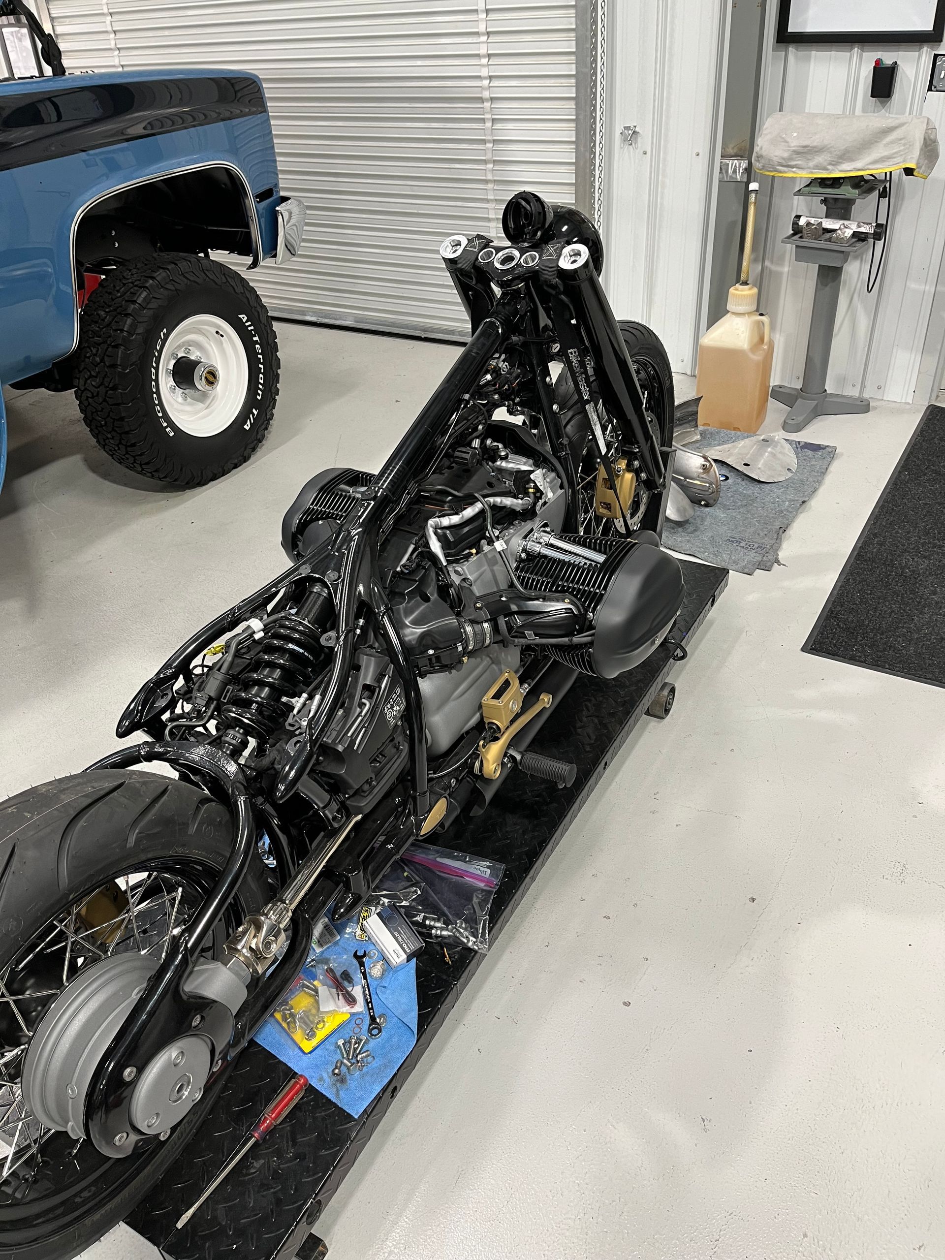 Black motorcycle frame on a shop floor beside a blue truck and garage equipment