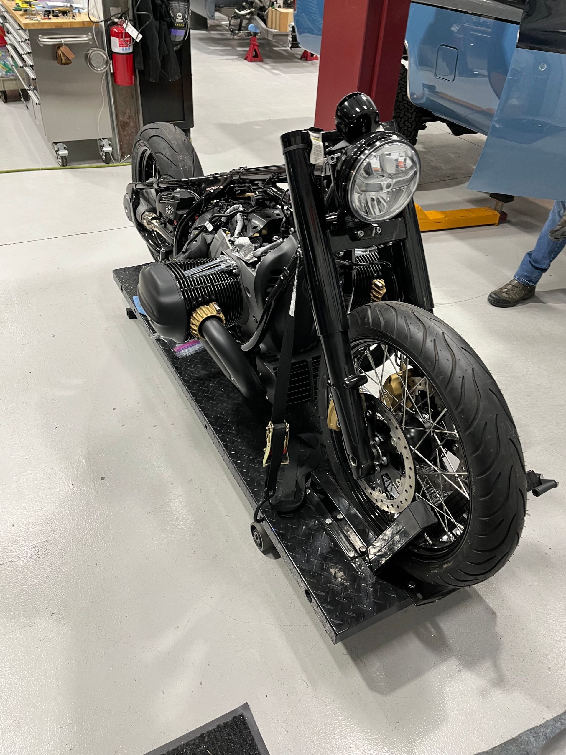 Damaged black motorcycle on a workshop floor, with exposed parts and debris around it.