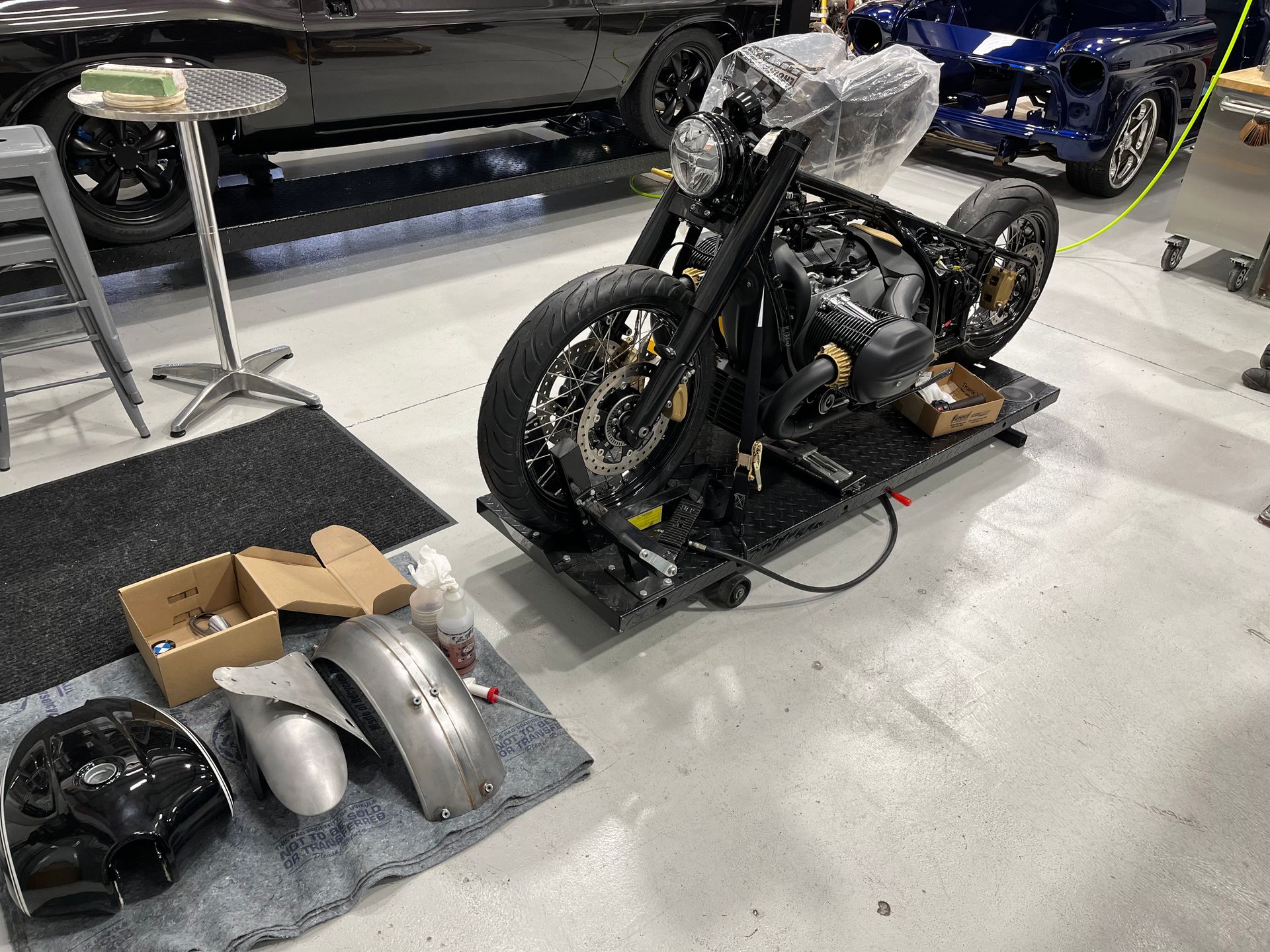 Custom motorcycle on display with loose body panels and parts on the floor in a garage-like showroom
