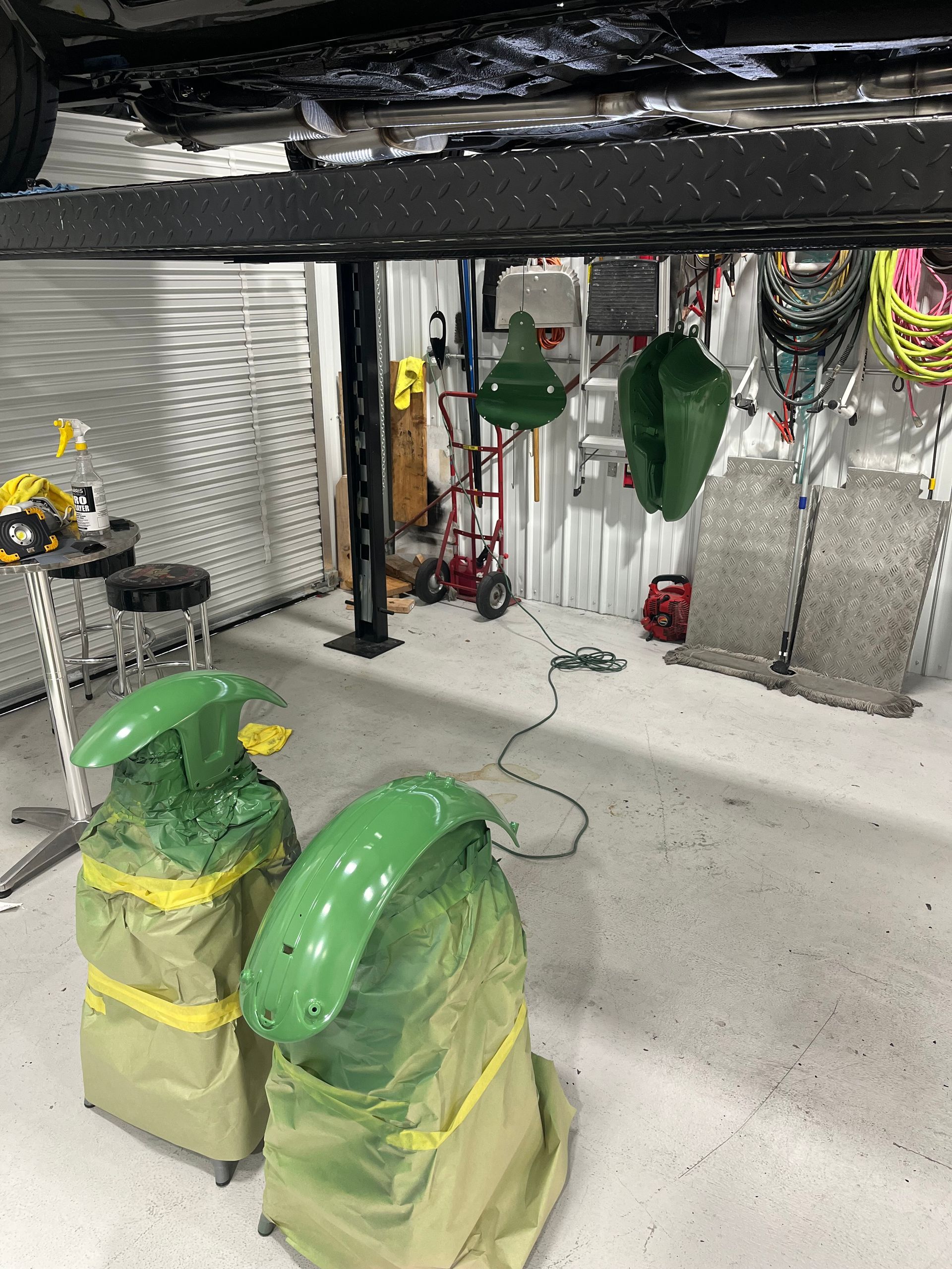 Indoor industrial workspace with green-covered equipment, metal structures, and hanging tools under a black overhead beam