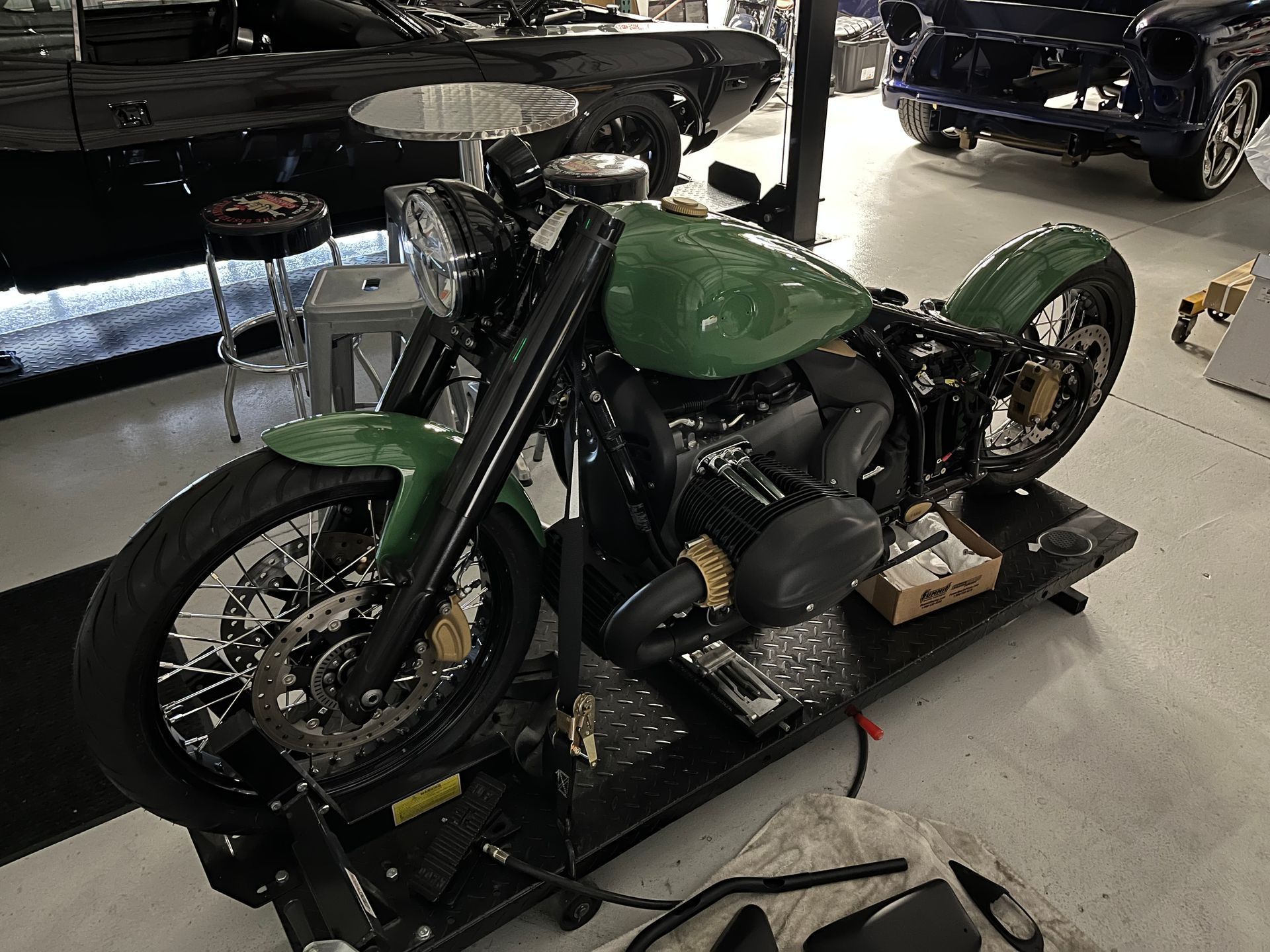 Green motorcycle displayed indoors on a black platform, with another bike visible in the background.