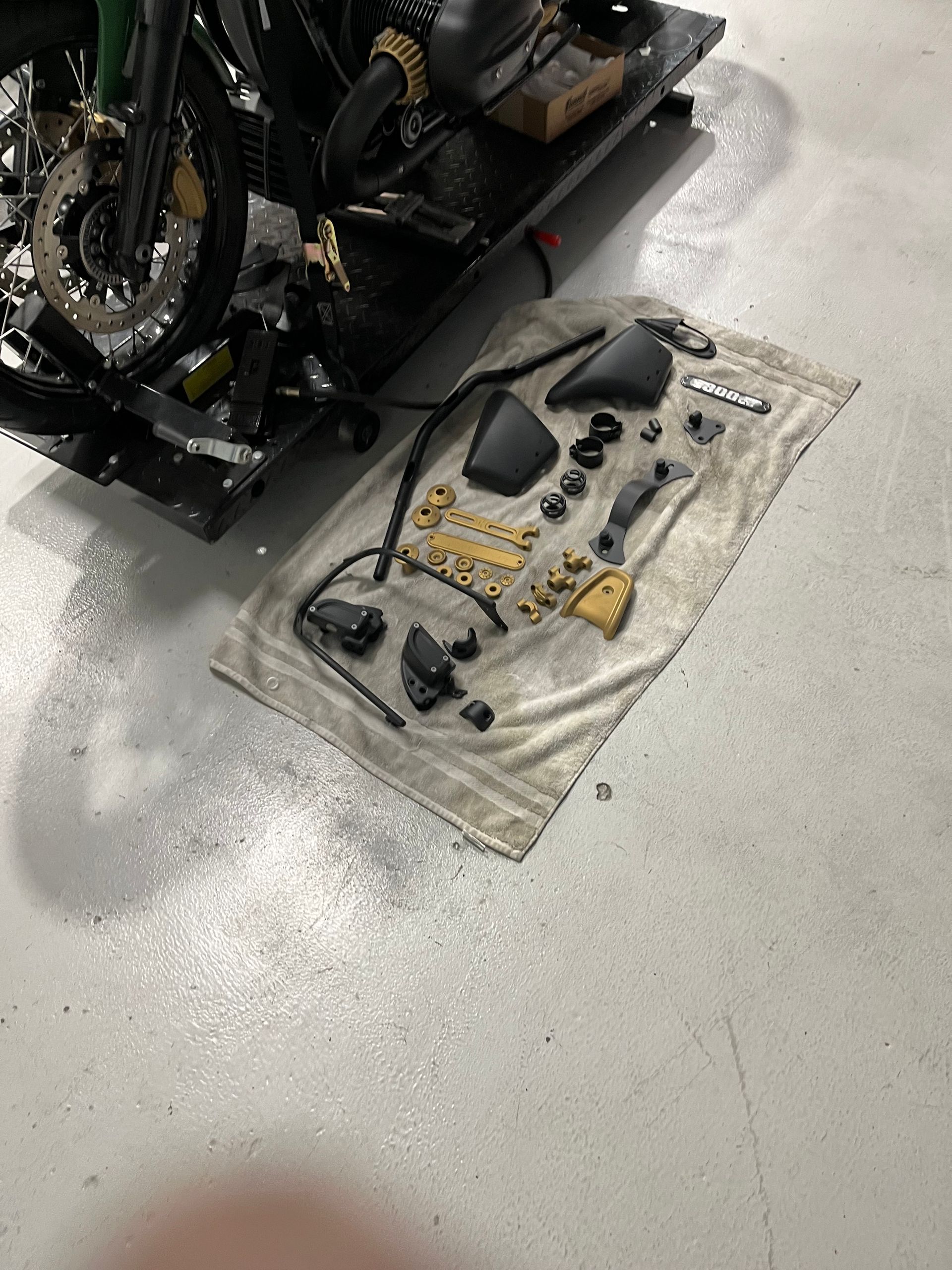 Tools and motorcycle parts laid out on a cloth beside a black motorcycle in a garage.
