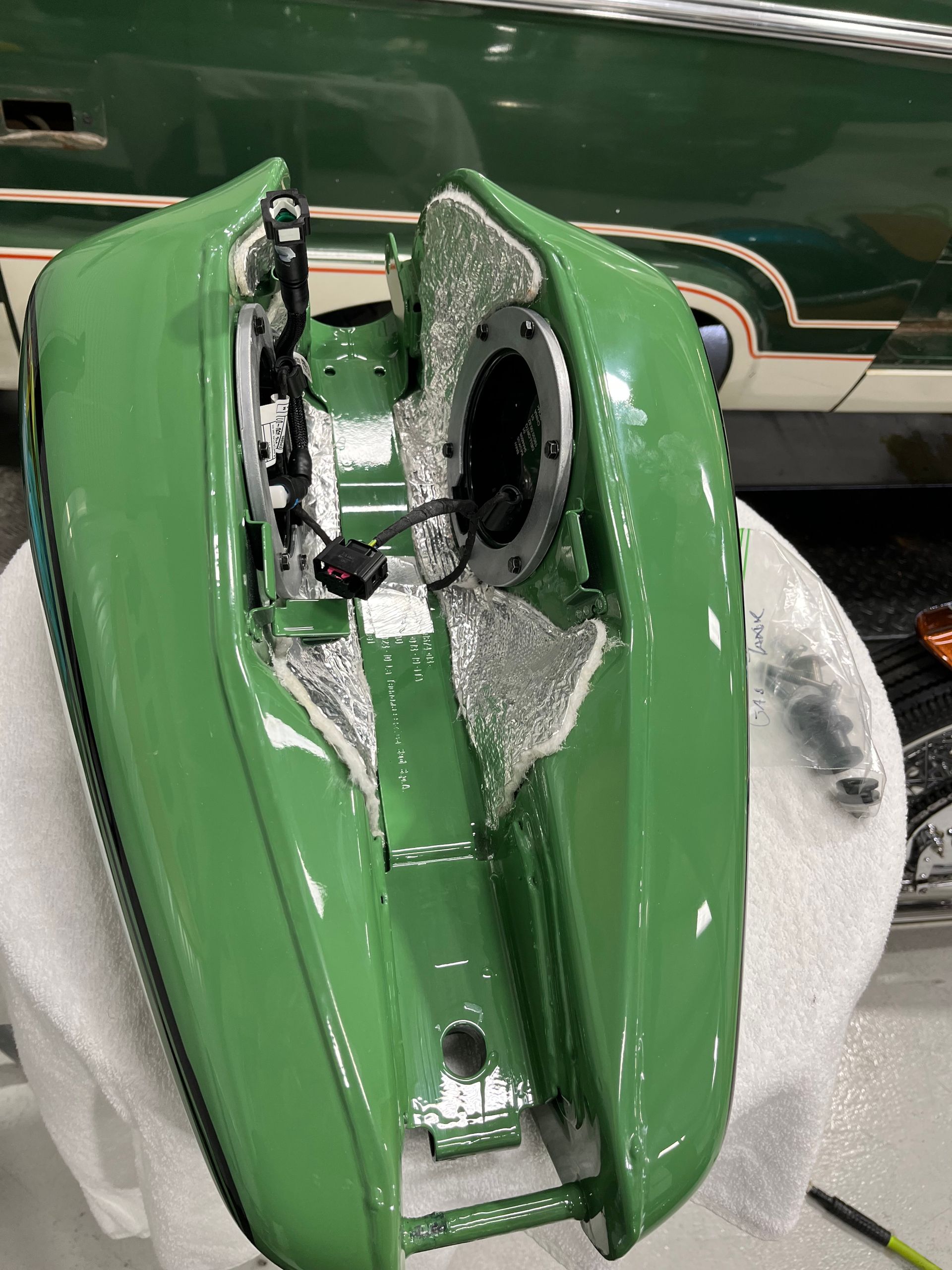 Green motorcycle fuel tank and parts covered in foam, lying on a workbench in a garage.
