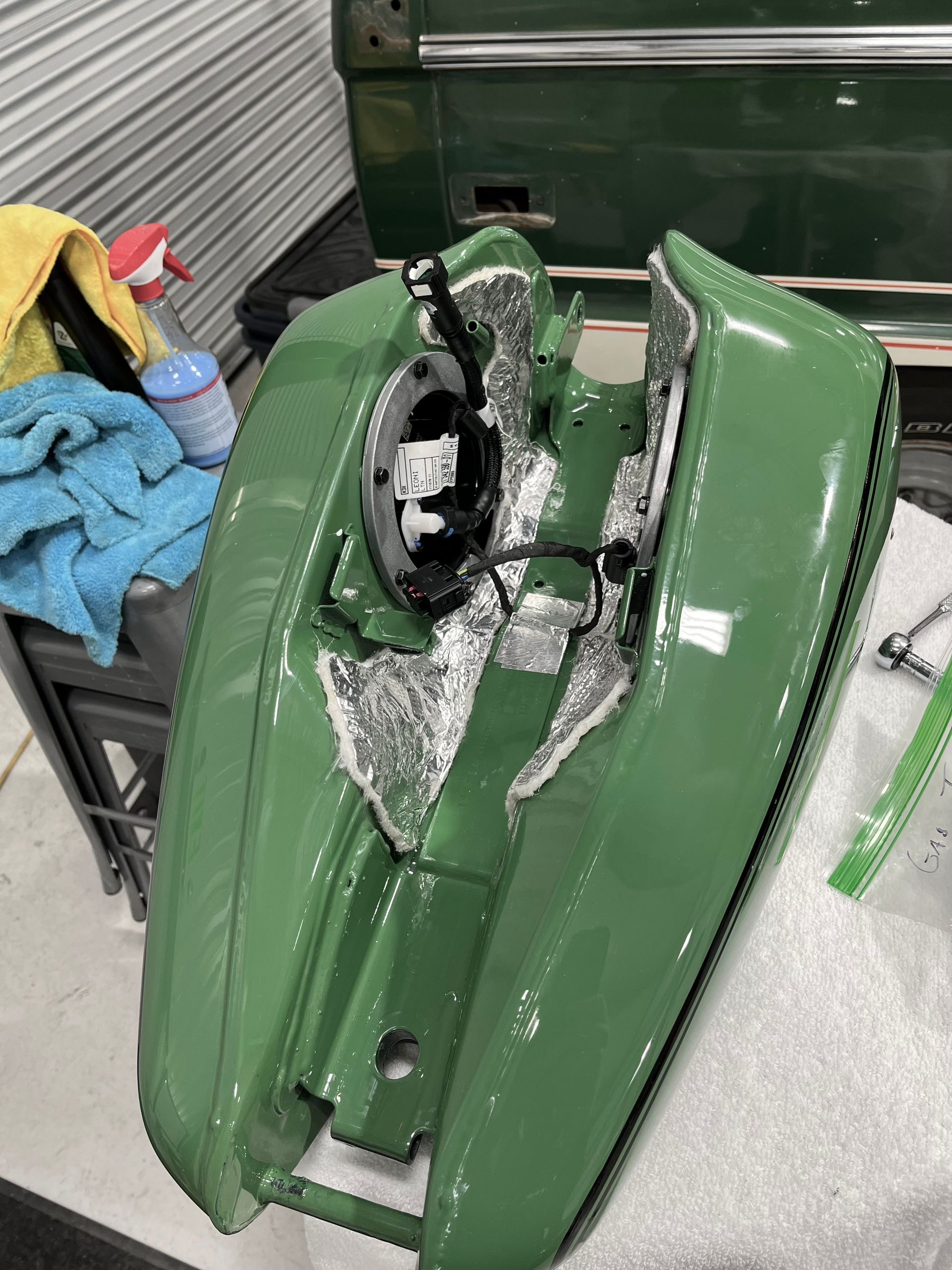 Severely damaged green car front end with crushed hood and exposed internal parts in a garage.