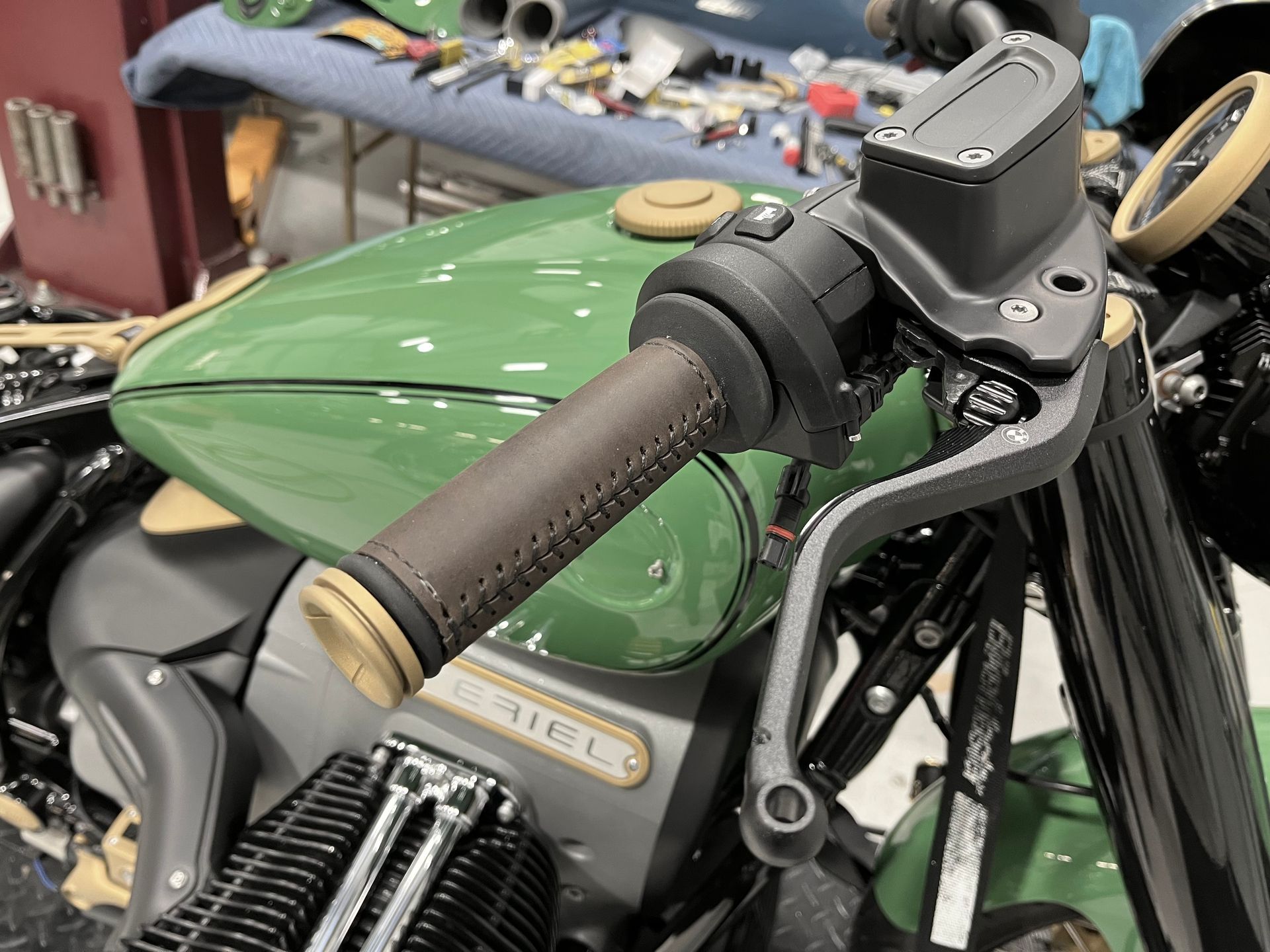 Close-up of a green motorcycle fuel tank and handlebar with brown grip in a workshop