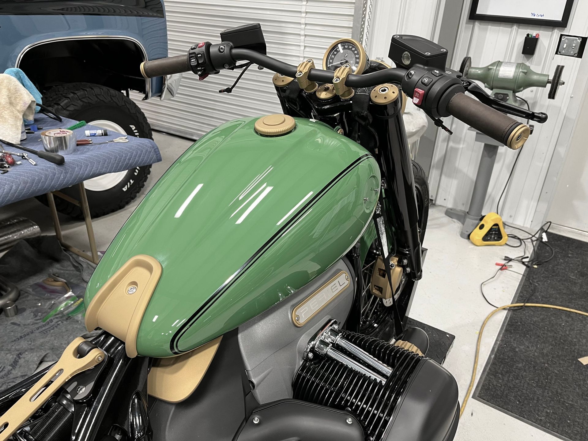 Green motorcycle in a garage, viewed from the front with black handlebars and tan accents.