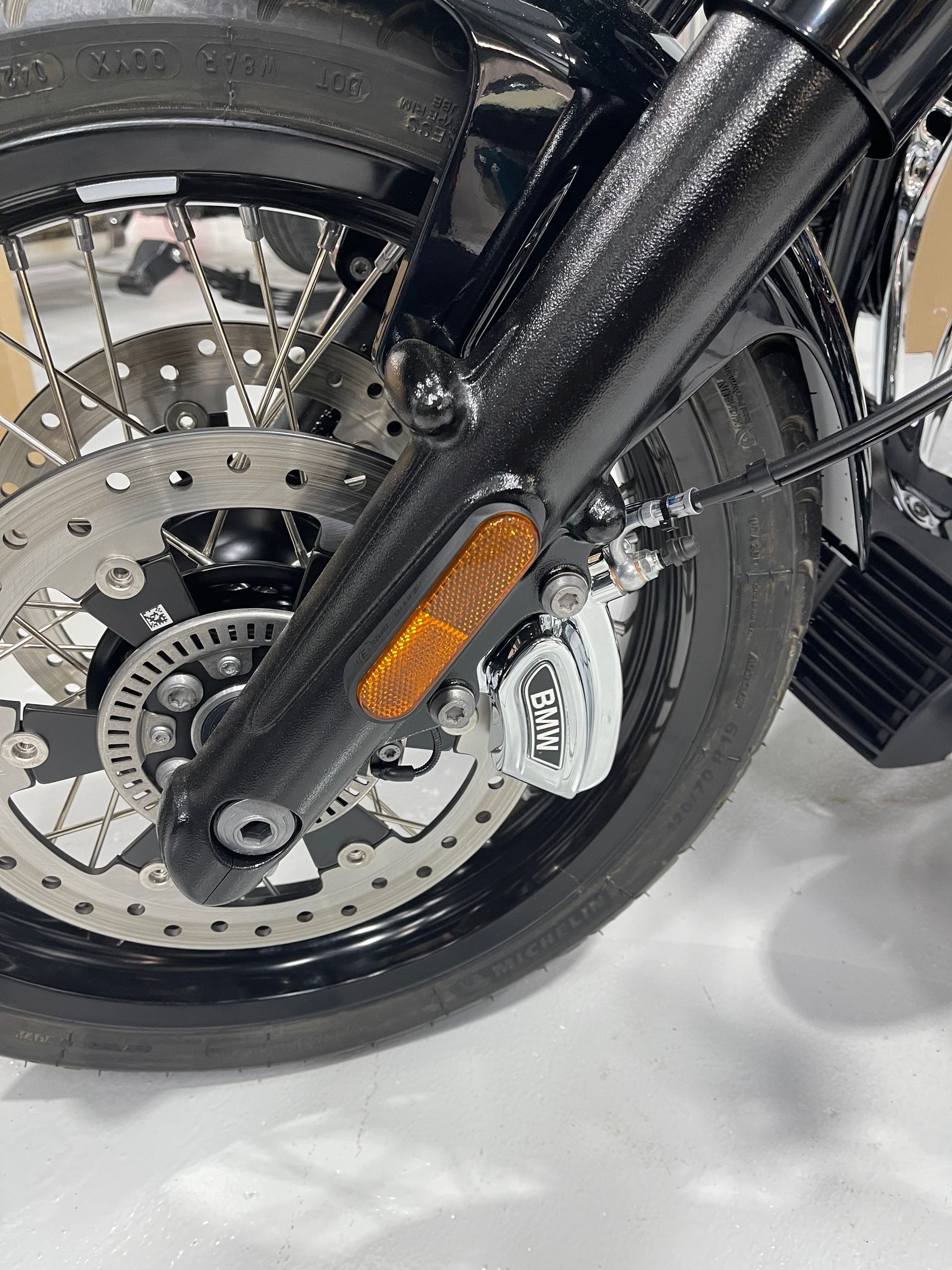Close-up of a motorcycle front wheel with disc brake, black tire, and amber reflector.