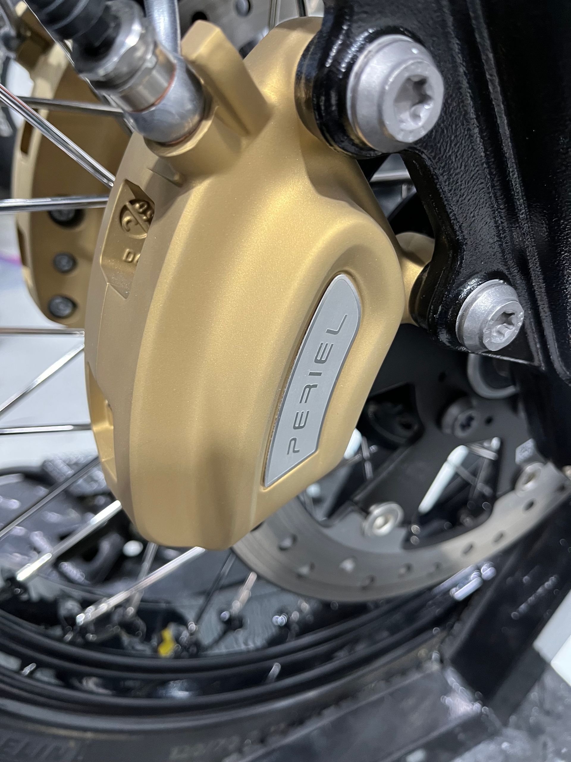 Close-up of a gold motorcycle brake caliper and disc with black wheel spokes