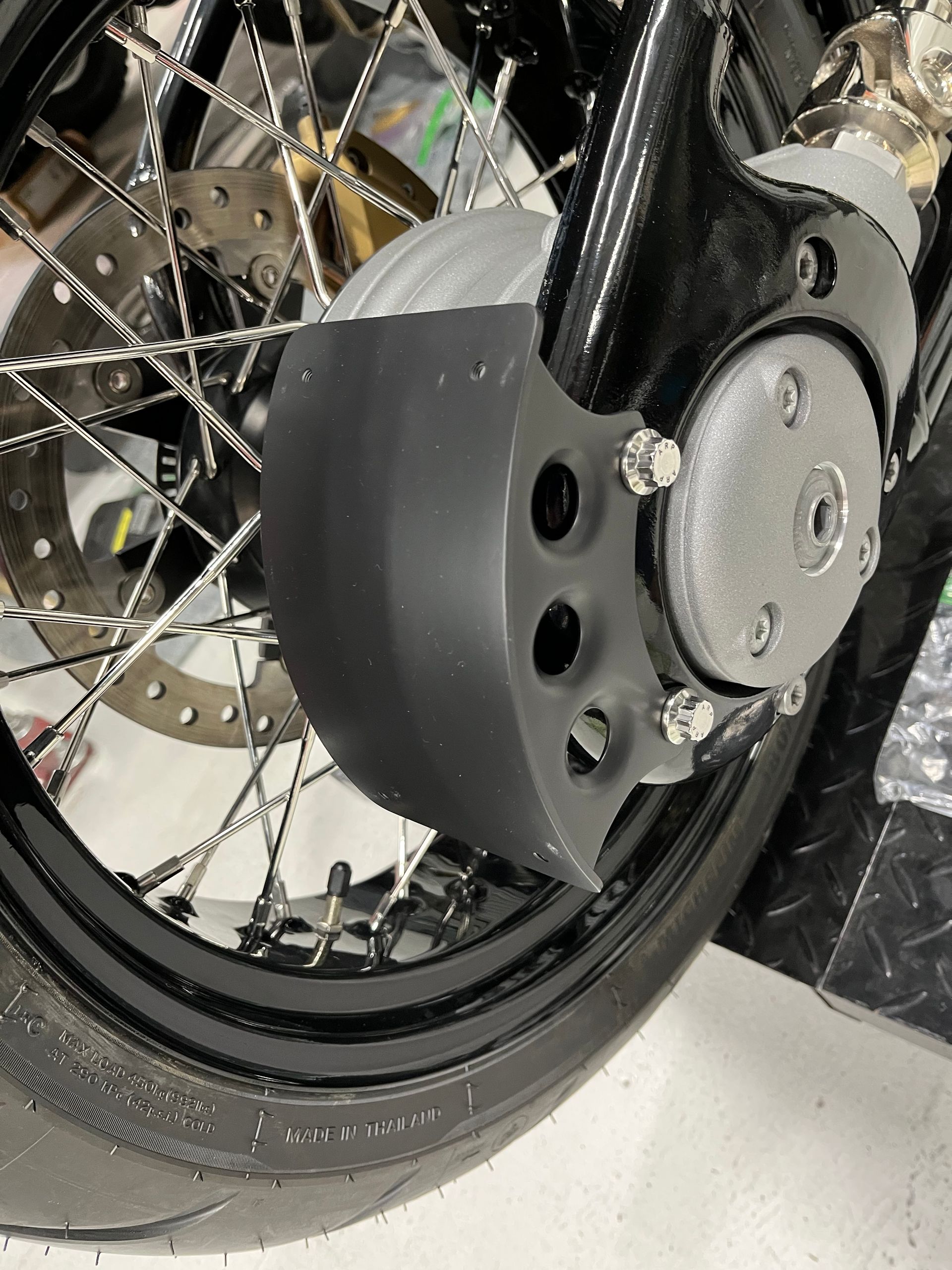 Close-up of a motorcycle wheel with black fender, spokes, and tire on a white floor