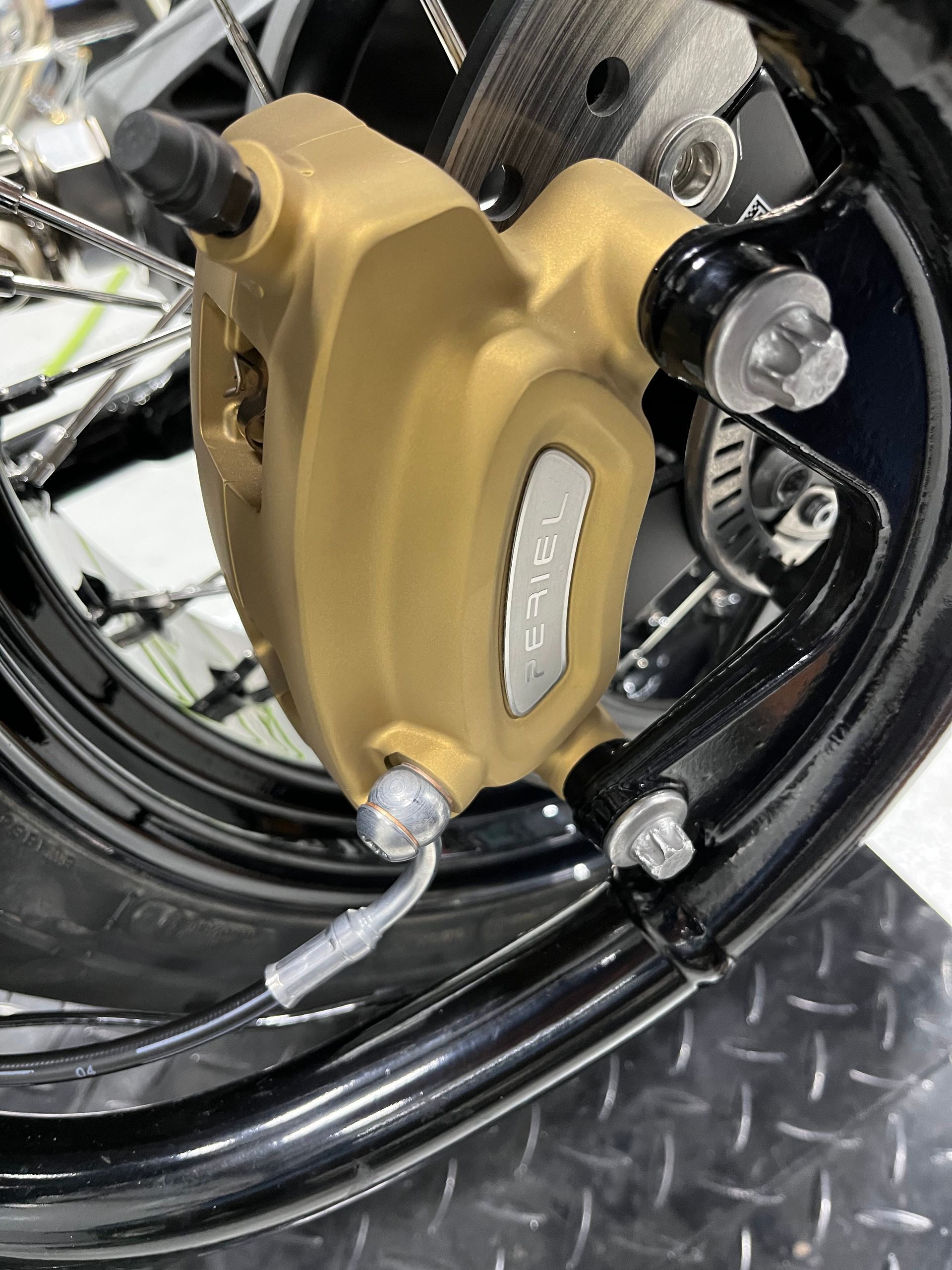 Gold brake caliper on a black wheel rim with silver bolts and braided hose