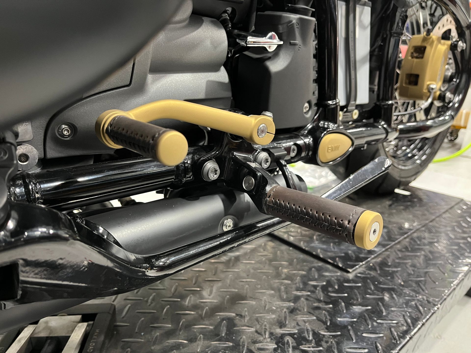 Close-up of a motorcycle’s black engine and exhaust with gold foot pegs on a metal platform.