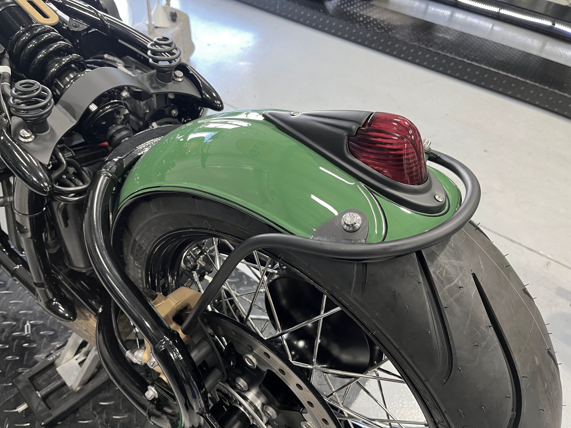 Green motorcycle rear fender with red taillight and wide tire in a showroom