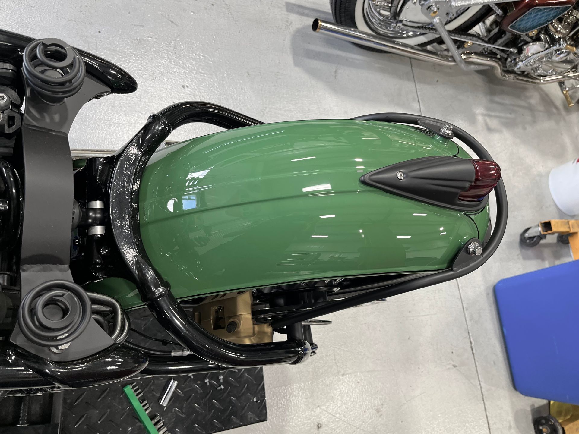 Green motorcycle fuel tank on a black frame in a workshop or garage.