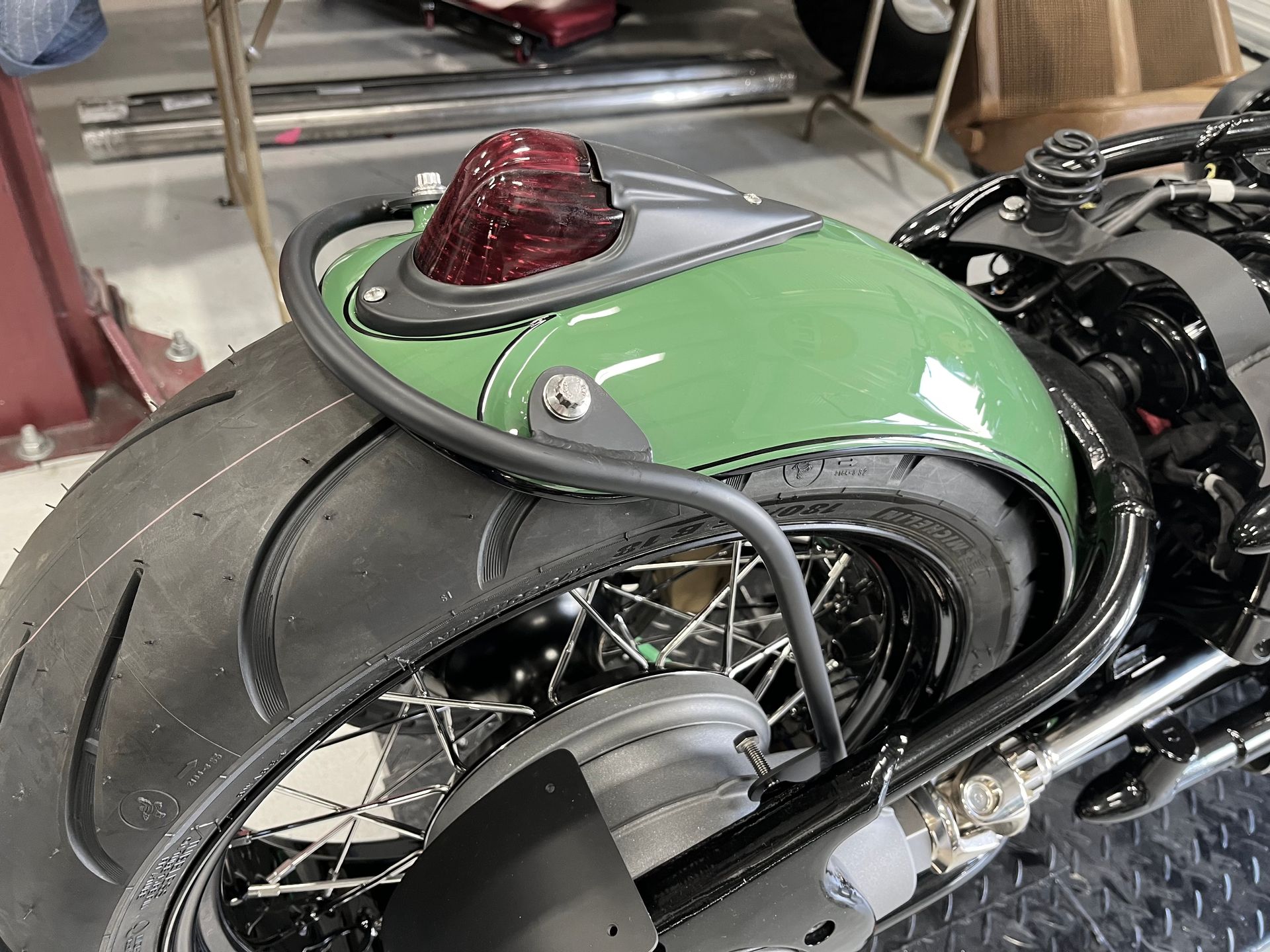 Green custom motorcycle rear seat and fender with a black tire in a workshop