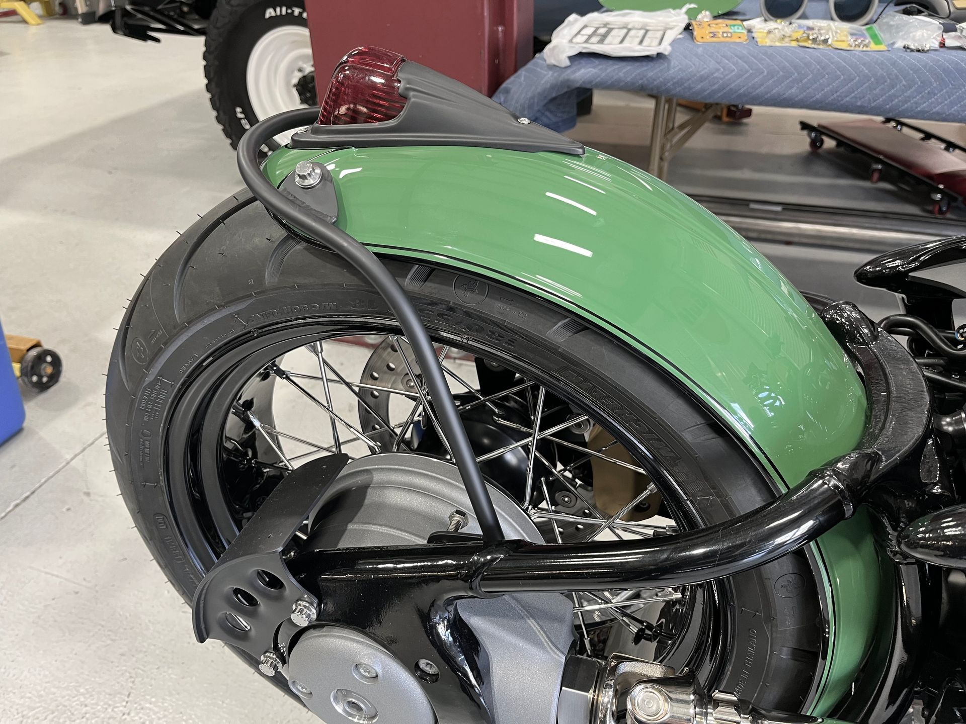 Green recumbent-style bicycle with a large black rear wheel and chrome spokes in a workshop.