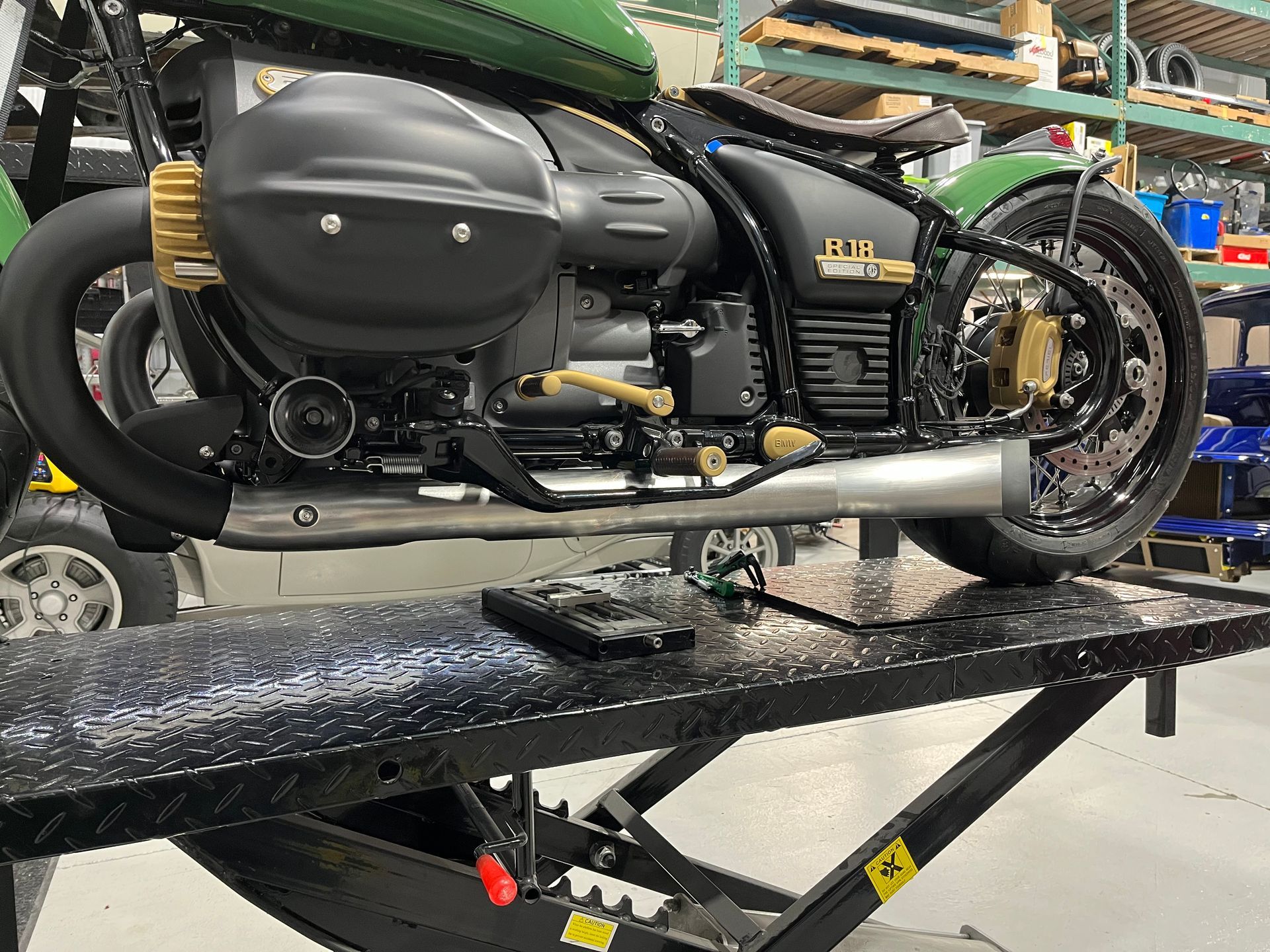 Black custom motorcycle on a lift in a workshop, side view with gold accents and silver exhaust.