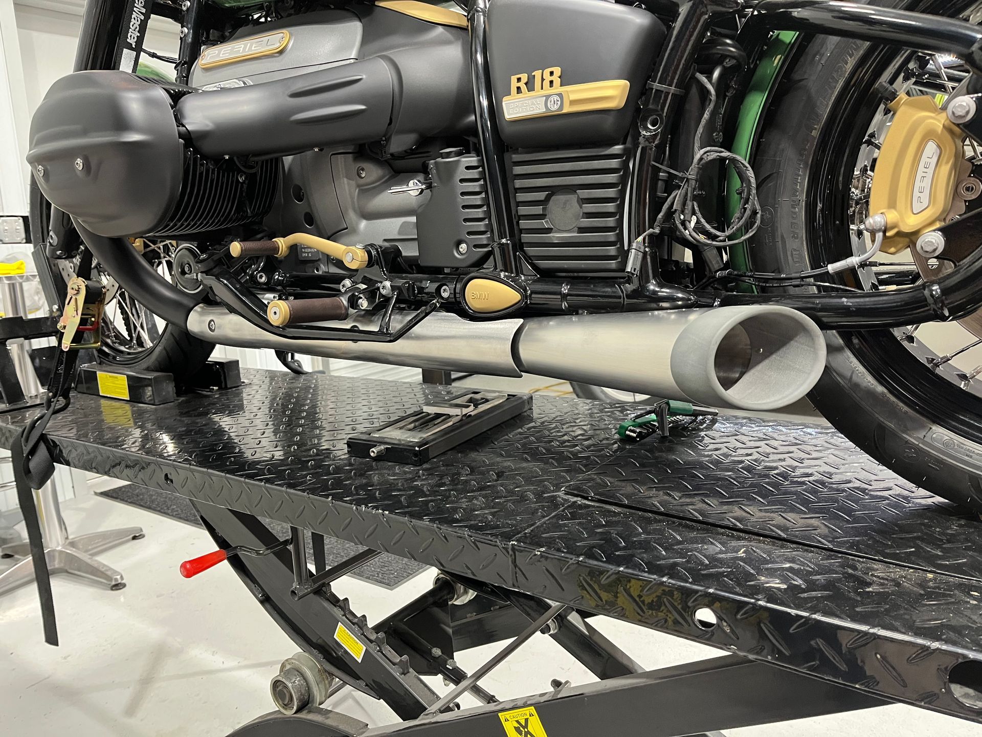 Black motorcycle on a lift, showing chrome exhaust and yellow engine details in a workshop