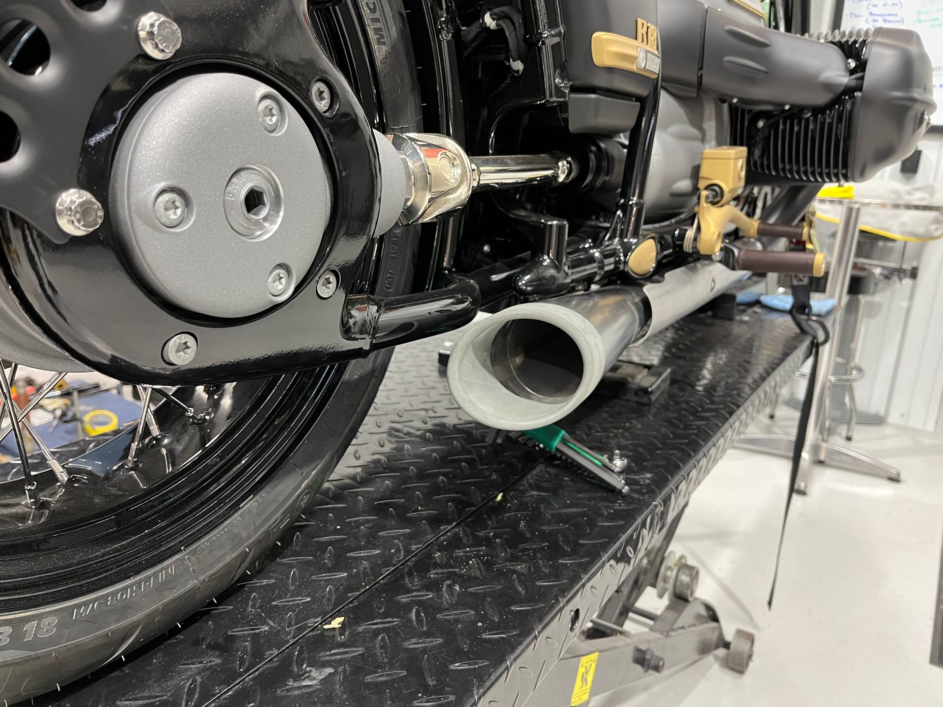 Close-up of a motorcycle’s rear side with chrome exhaust pipe and black wheel on a display stand