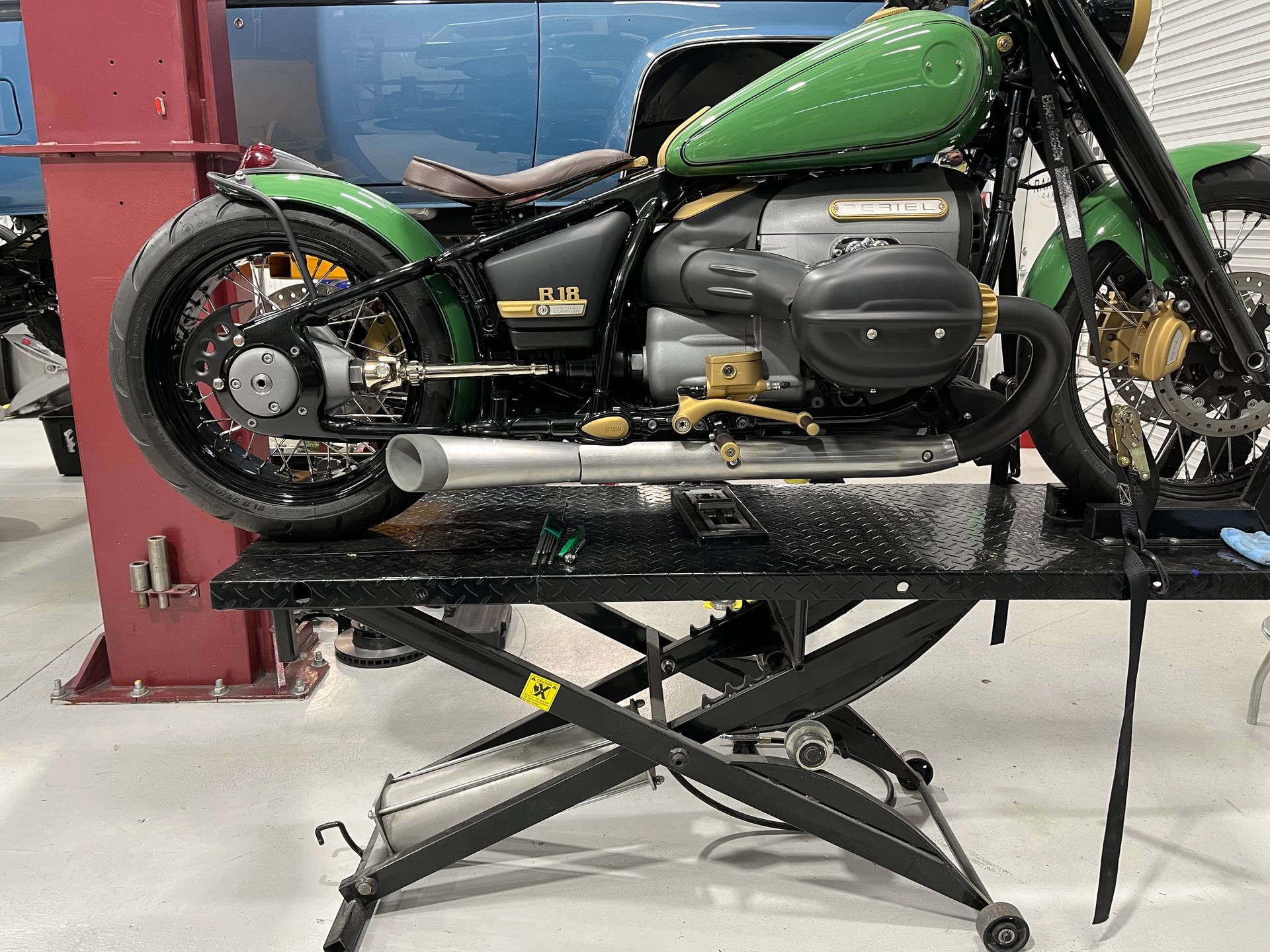 Custom green motorcycle on a lift in a garage, showing the rear wheel and engine.
