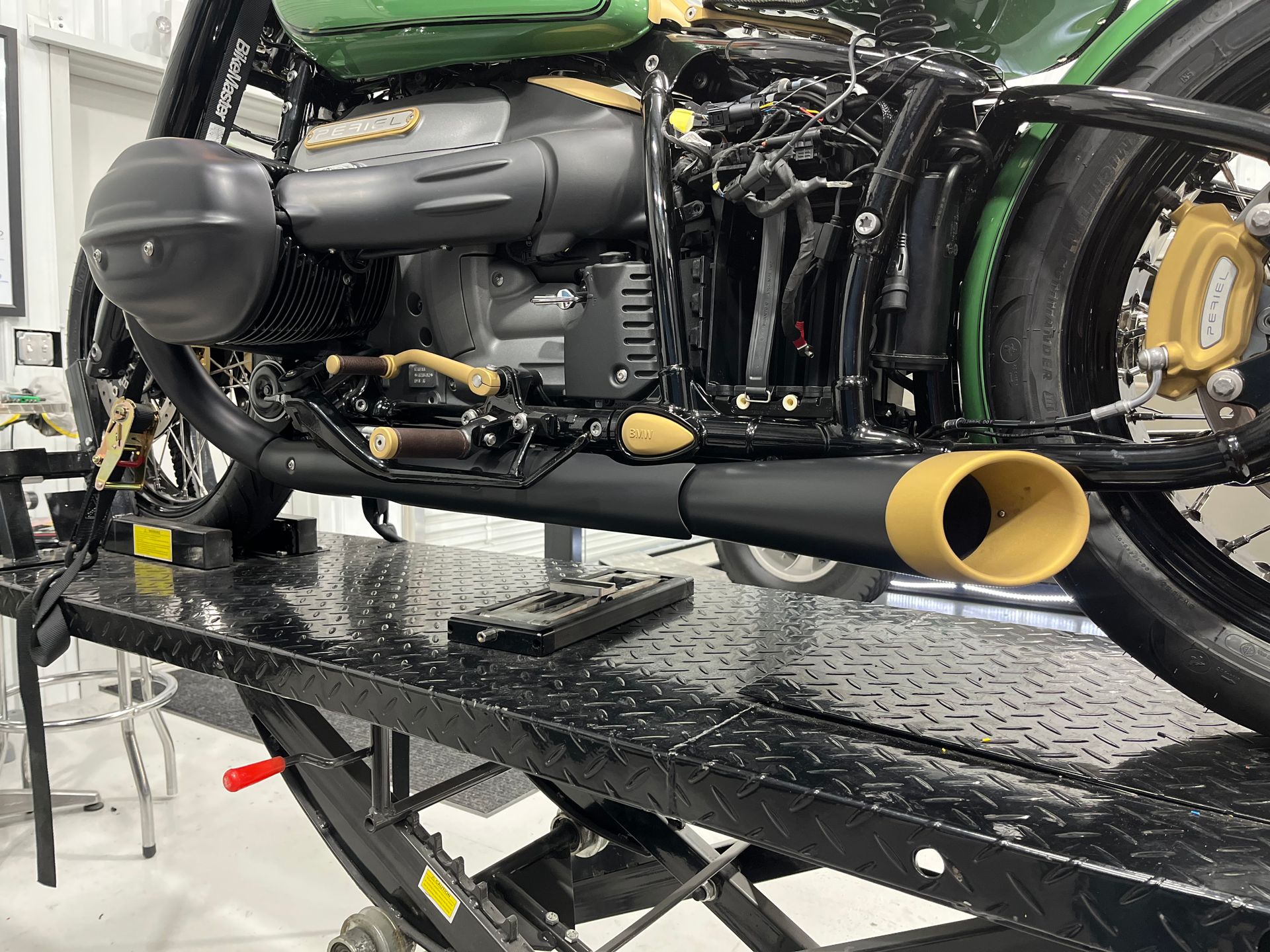 Black motorcycle on a wet metal lift, side view with exposed engine and yellow exhaust tips.