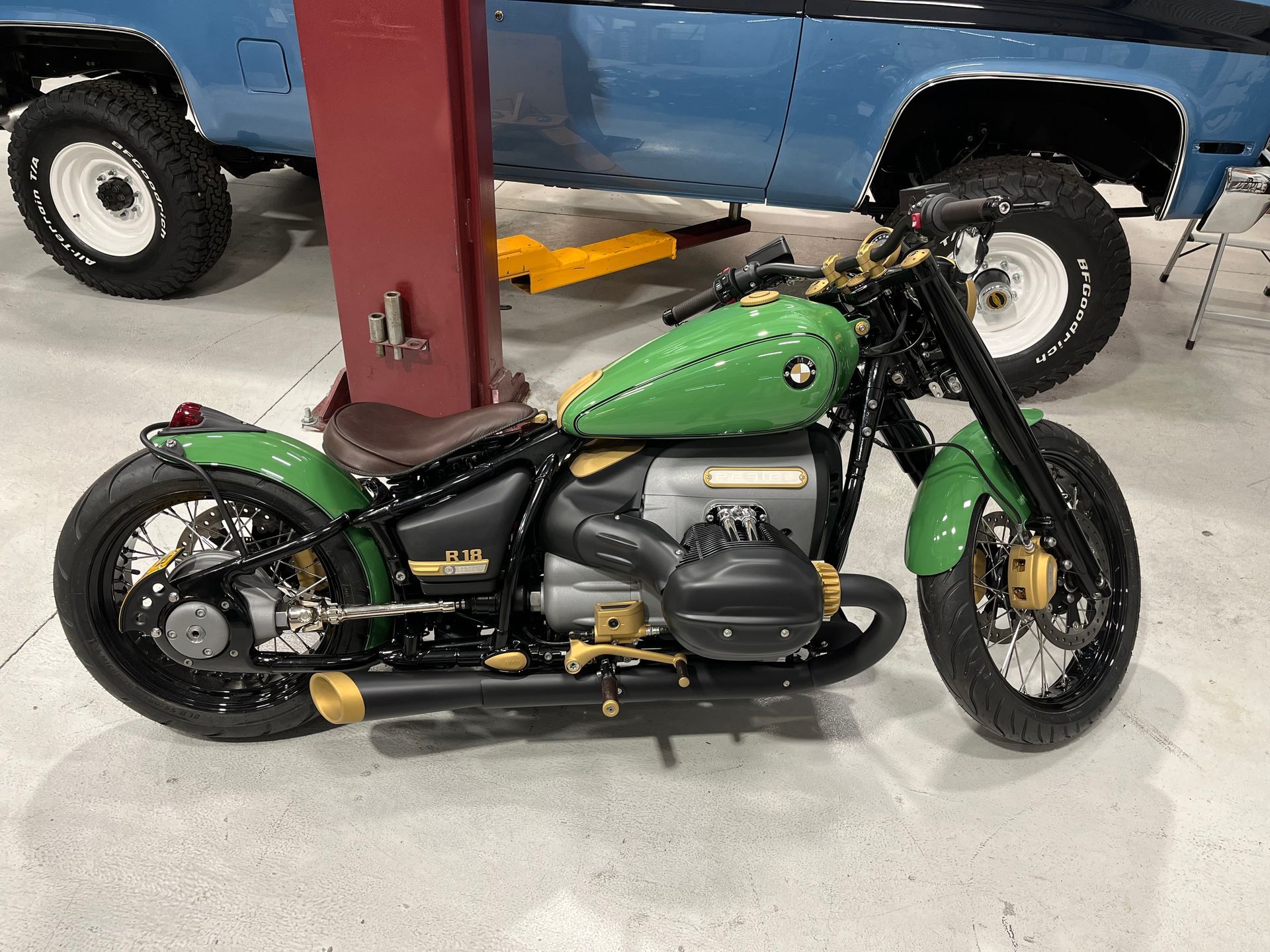 Green custom motorcycle in a garage, parked beside a lift and a blue pickup truck.