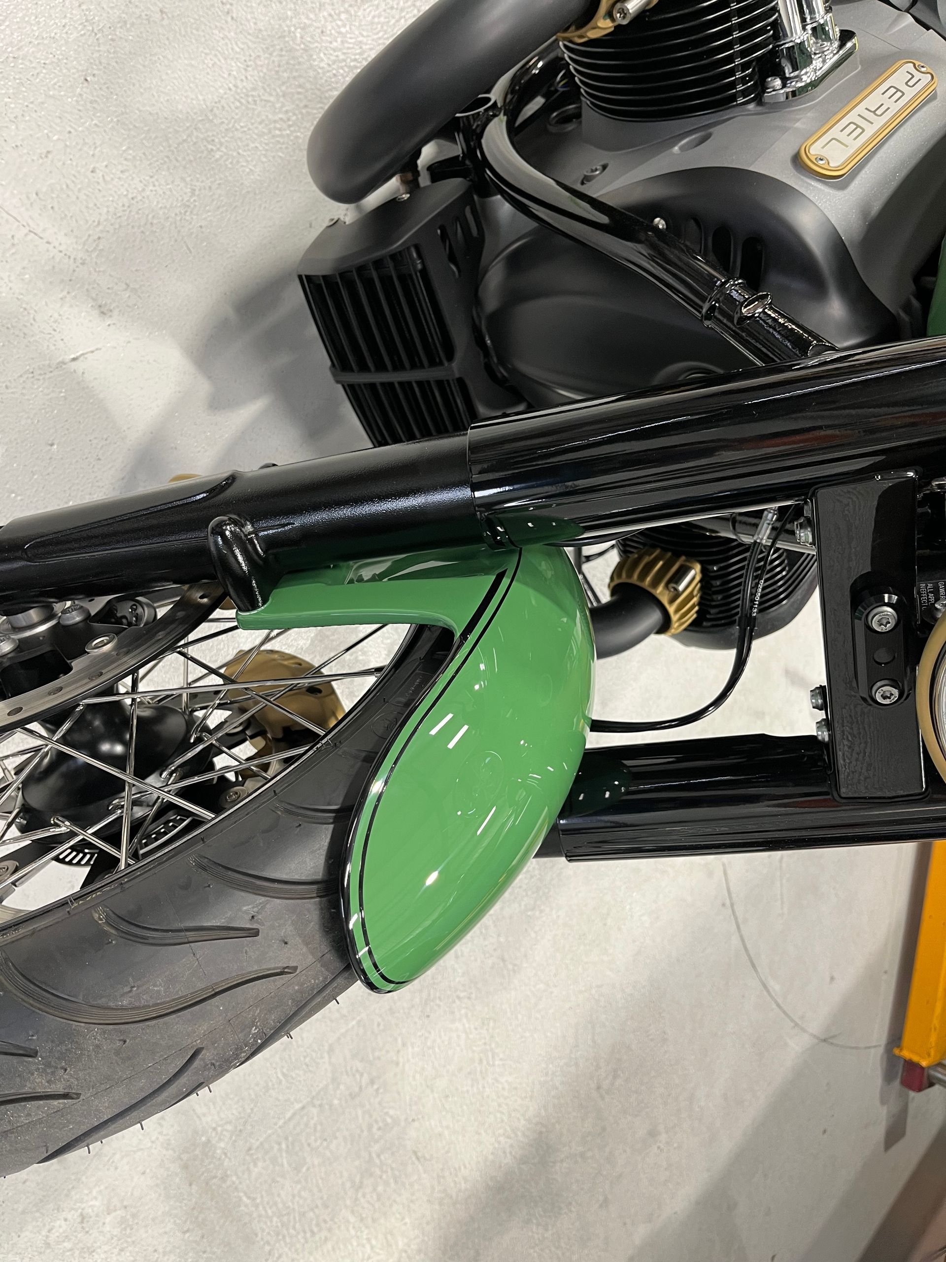 Green-front-fender motorcycle close-up with black frame and chrome wheel in a garage-like setting