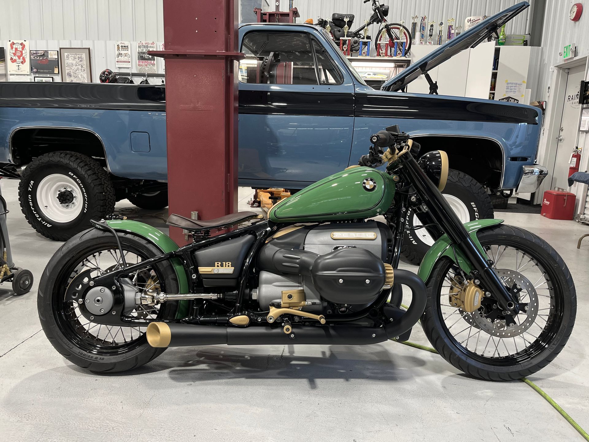 Green custom motorcycle in a garage, side view, with a blue pickup truck in the background.
