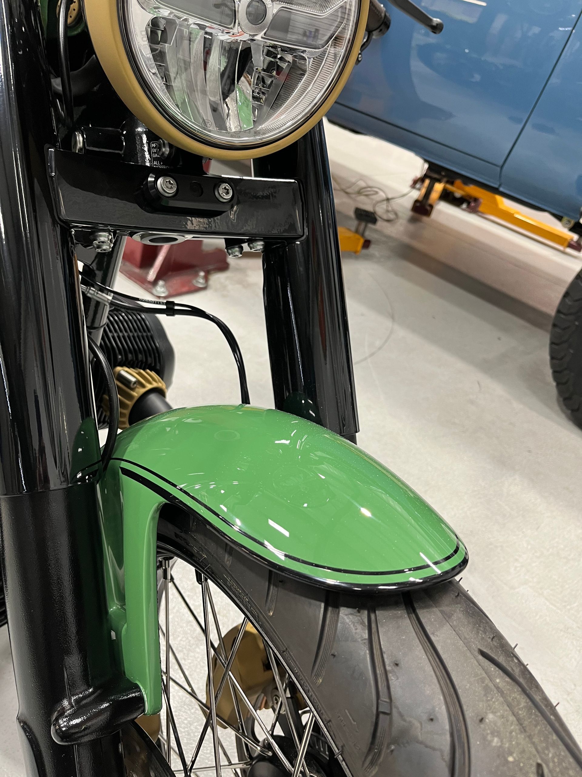 Close-up of a vintage bicycle front wheel, green fender, and headlight in a workshop.
