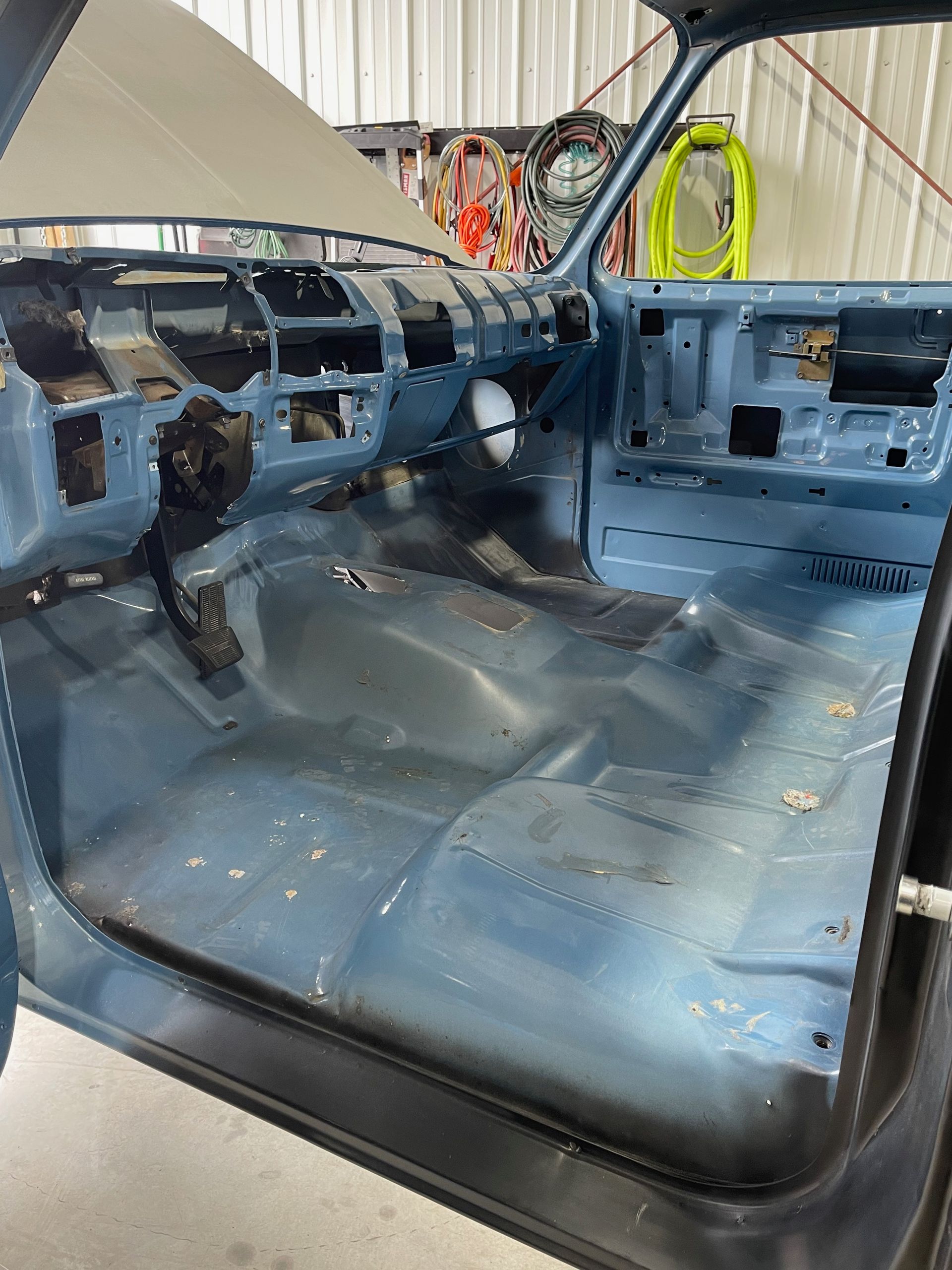 Interior of a stripped blue car cab with missing dashboard and seats, viewed from the open driver door