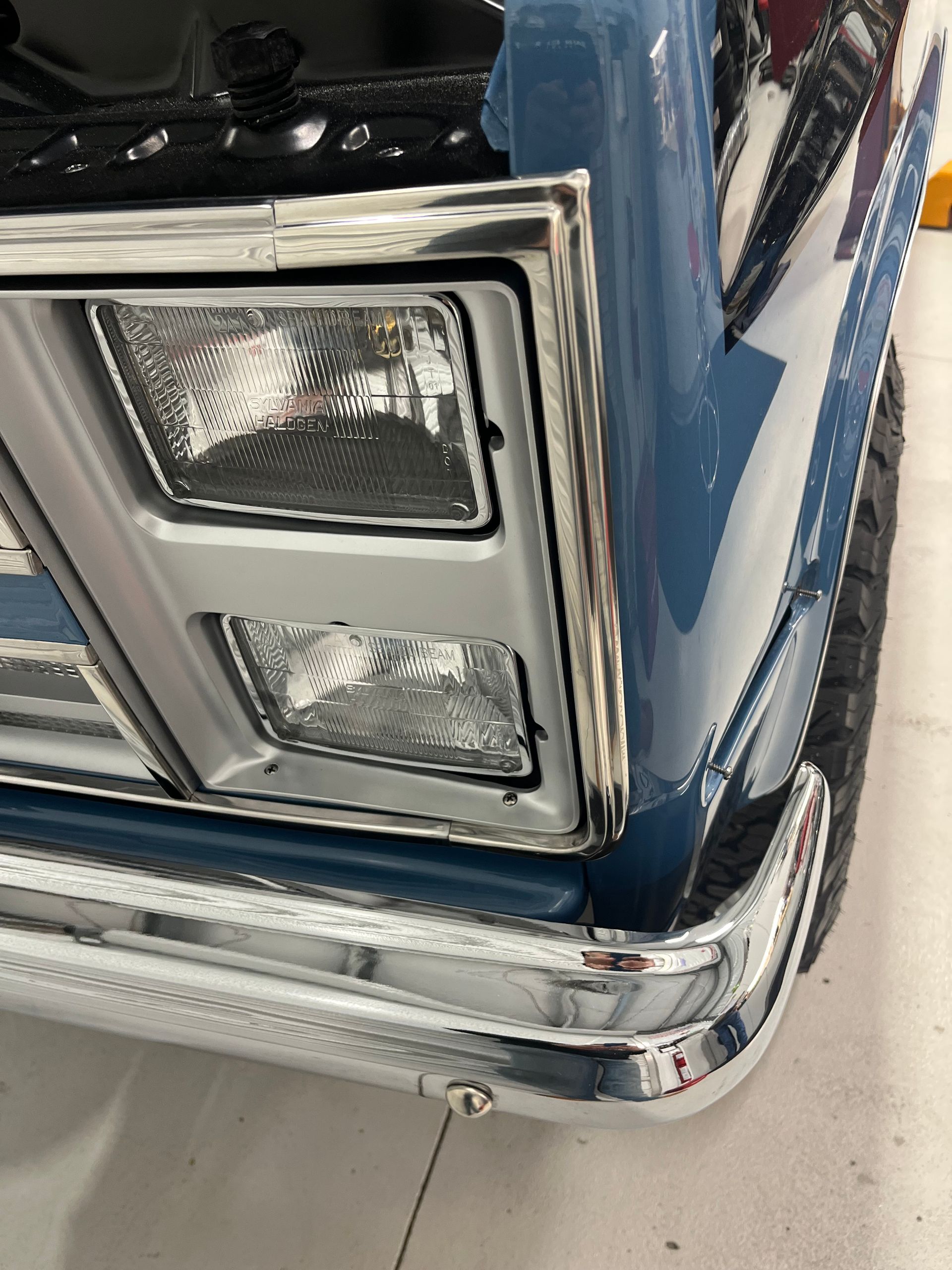 Close-up of a blue vintage car’s chrome front corner and headlight assembly