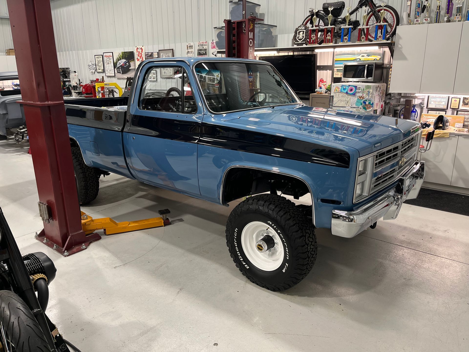 Blue lifted pickup truck in a workshop, parked beside a vehicle lift.