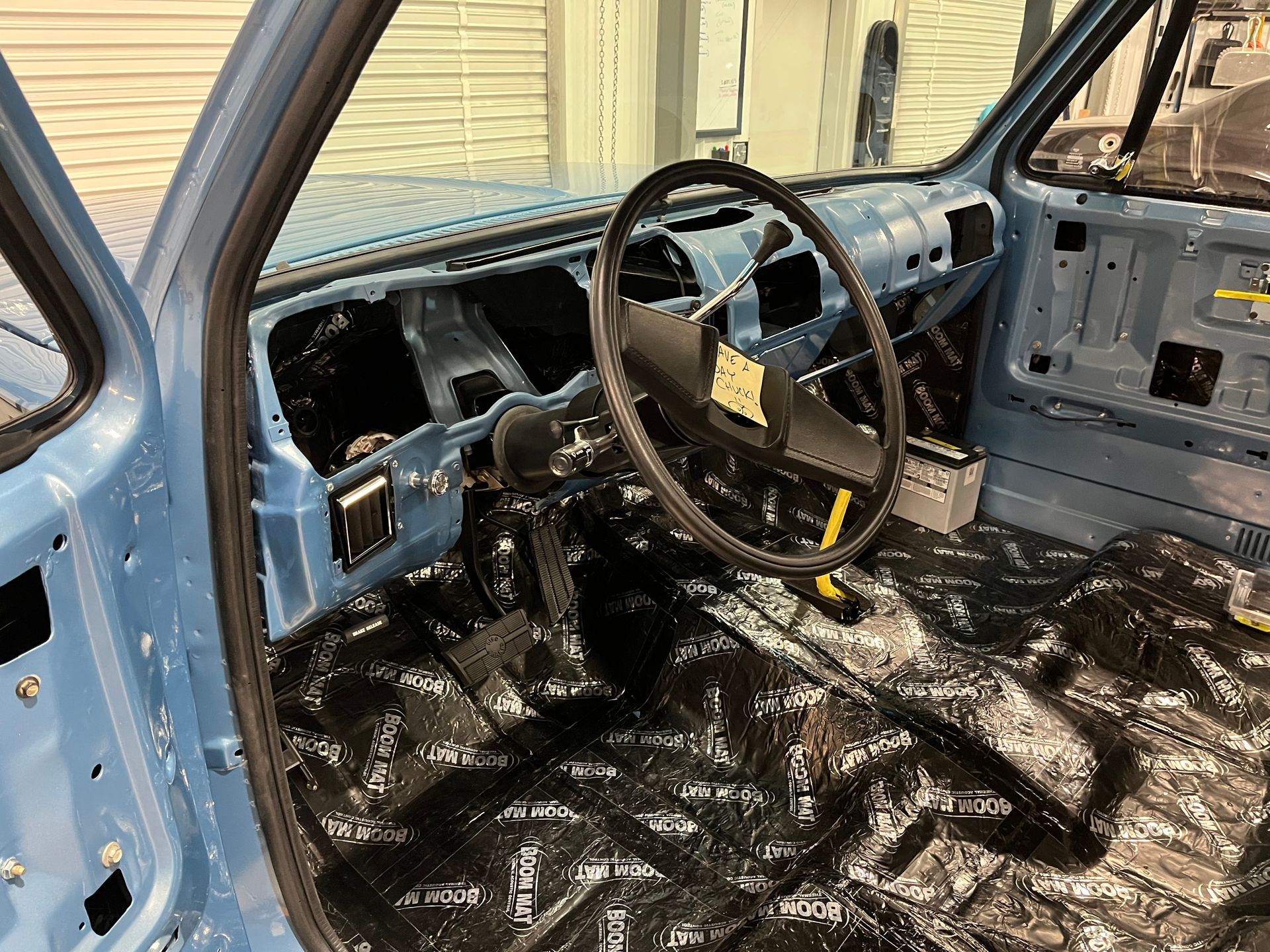 Damaged blue car interior with missing dashboard and debris-strewn floor, steering wheel intact.