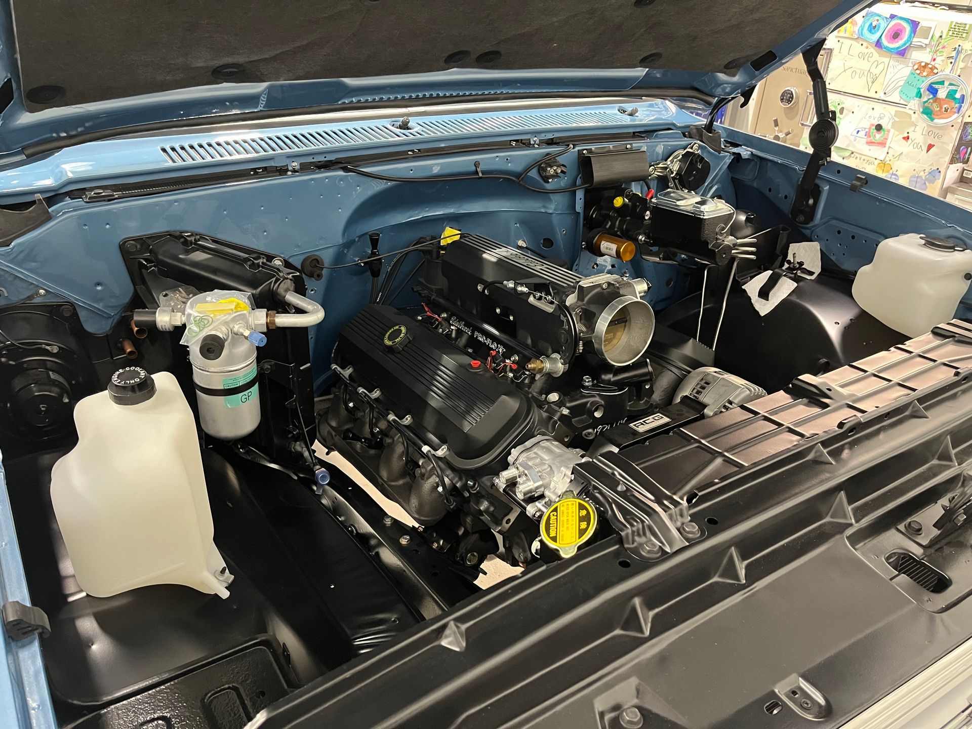 Car engine bay with a black engine, open hood, and visible fluid reservoirs and hoses