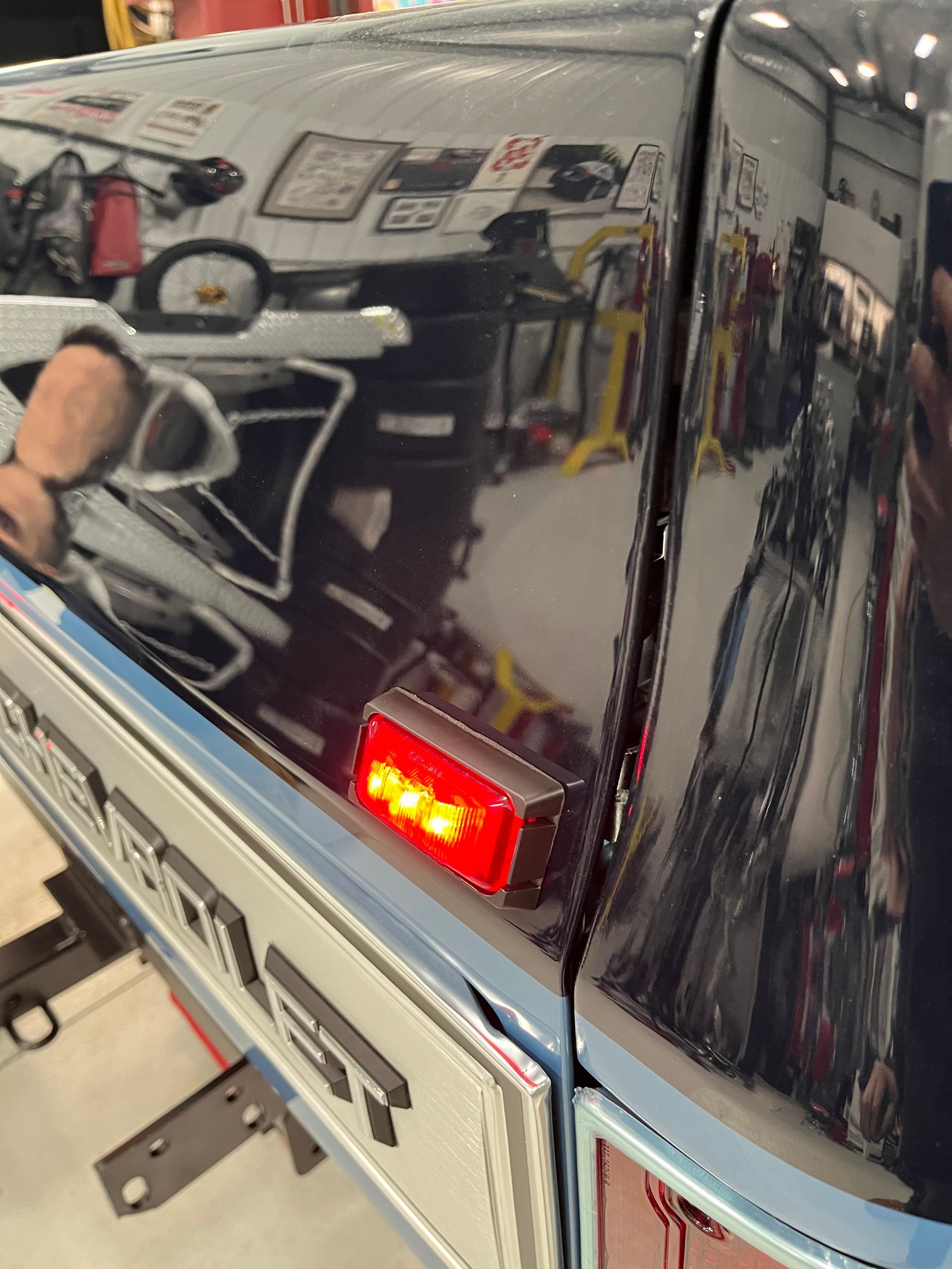 Close-up of a glossy black truck’s rear corner with a lit red taillight in a garage.
