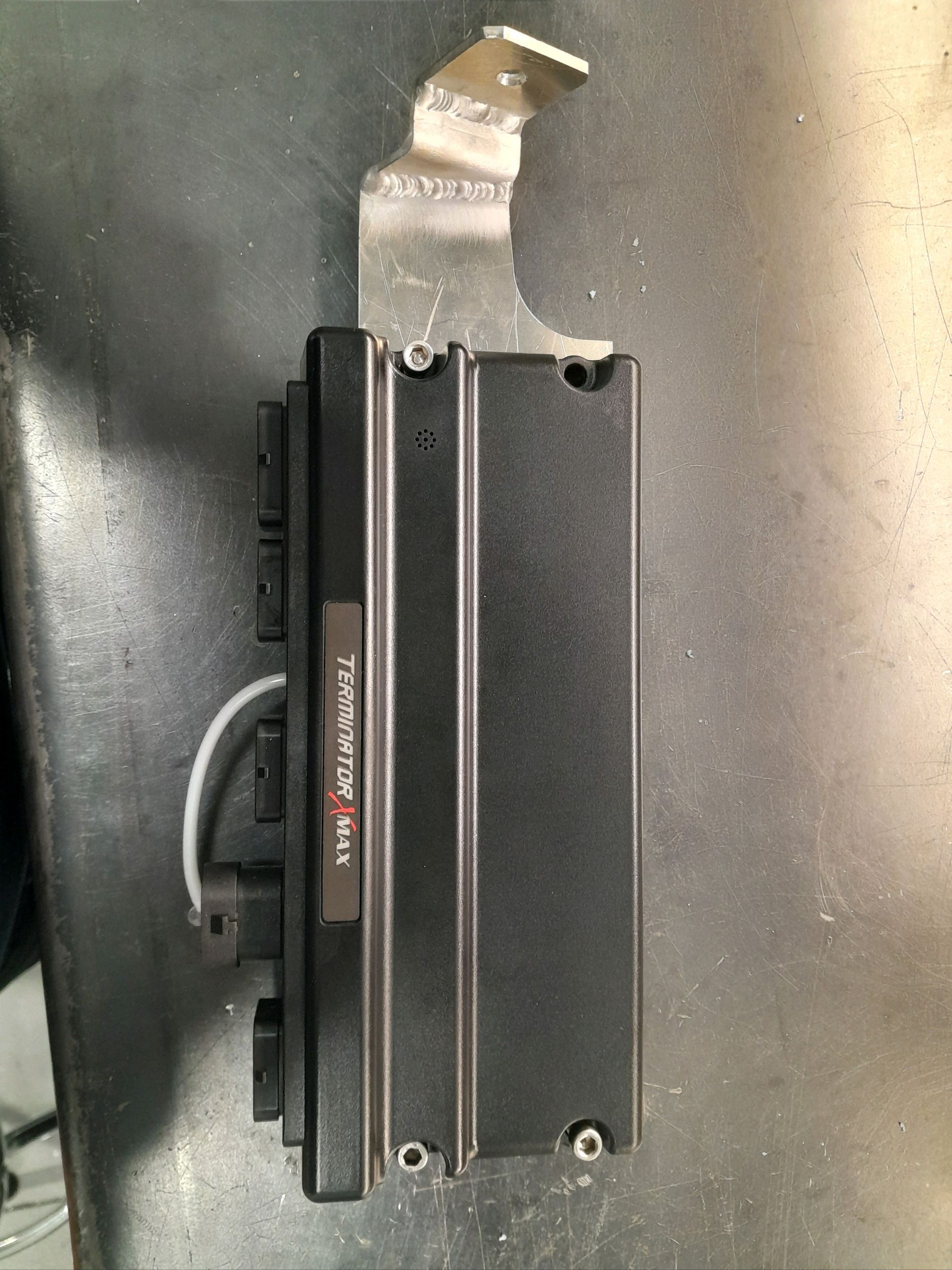 Black metal device with a silver mounting bracket on a dark tabletop, viewed from above.