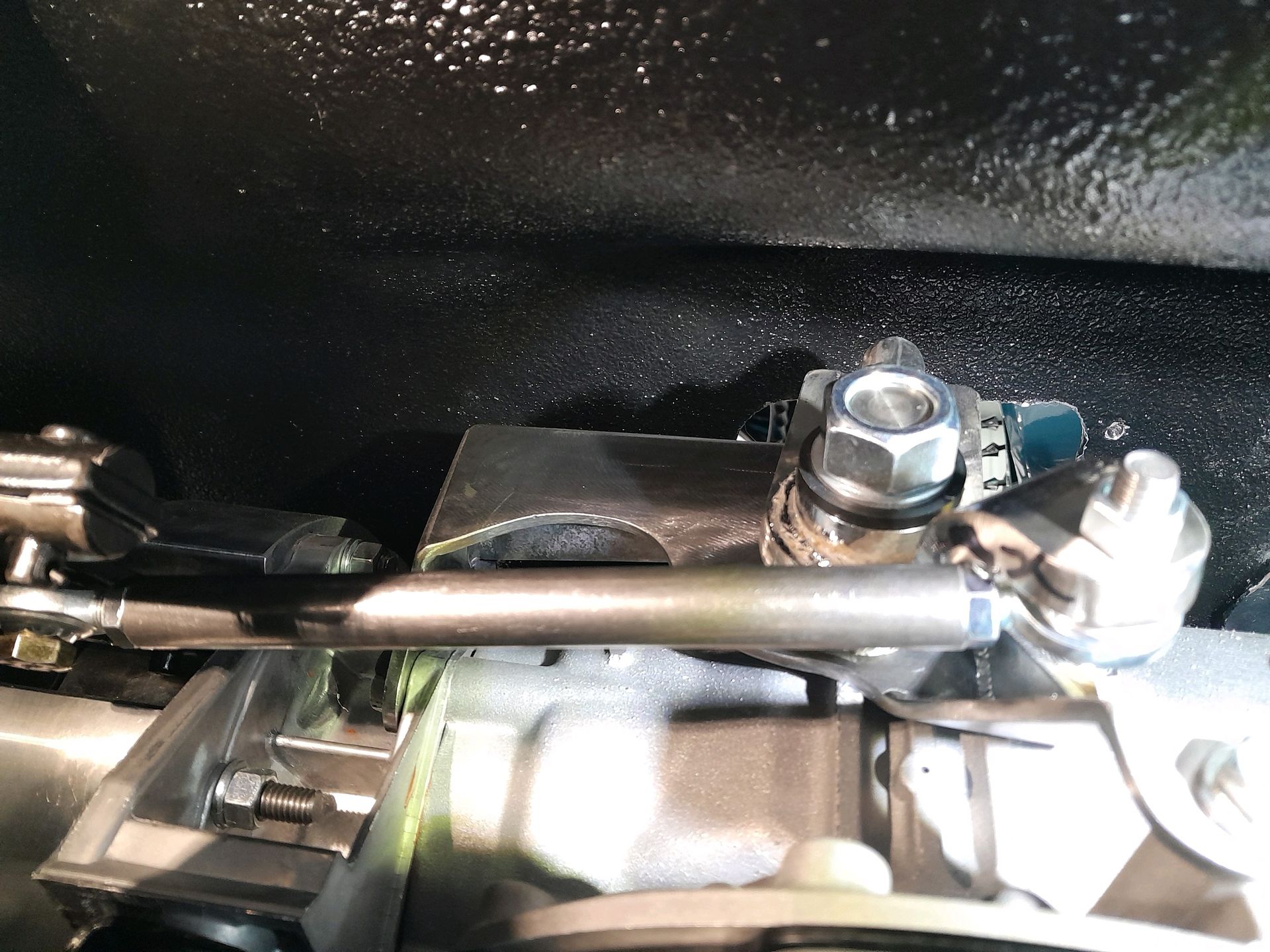 Close-up of a metallic mechanical linkage with bolts and rods inside a dark engine compartment