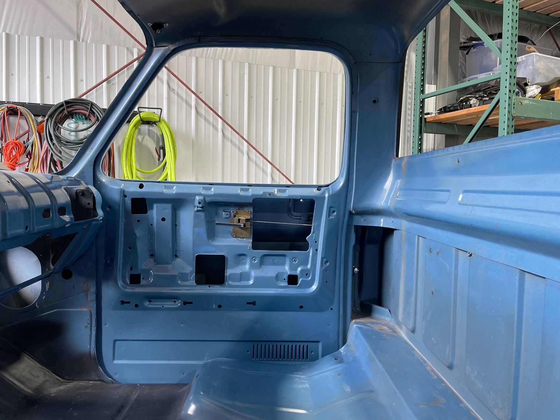 Blue-painted vehicle interior in a garage, showing bare metal cab walls and open side panels.