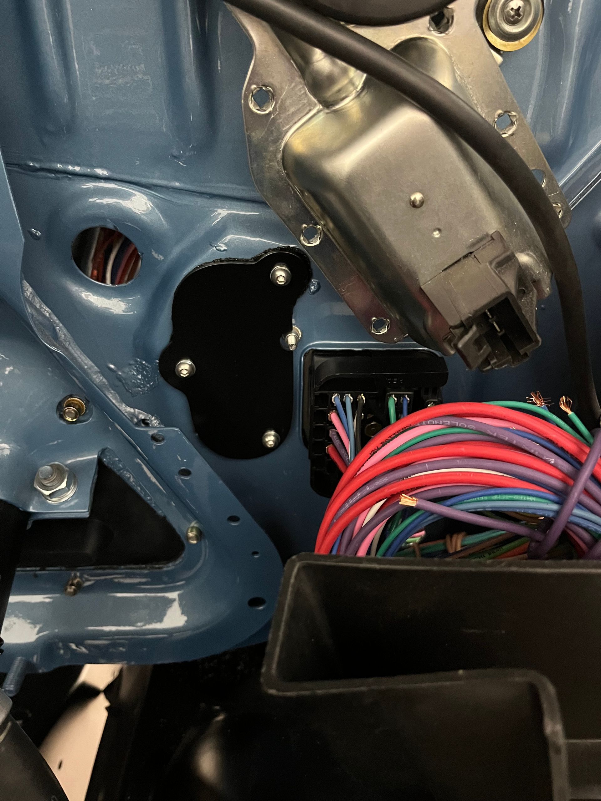 Close-up of a car door interior with blue metal, wiring harnesses, and a black electrical connector.