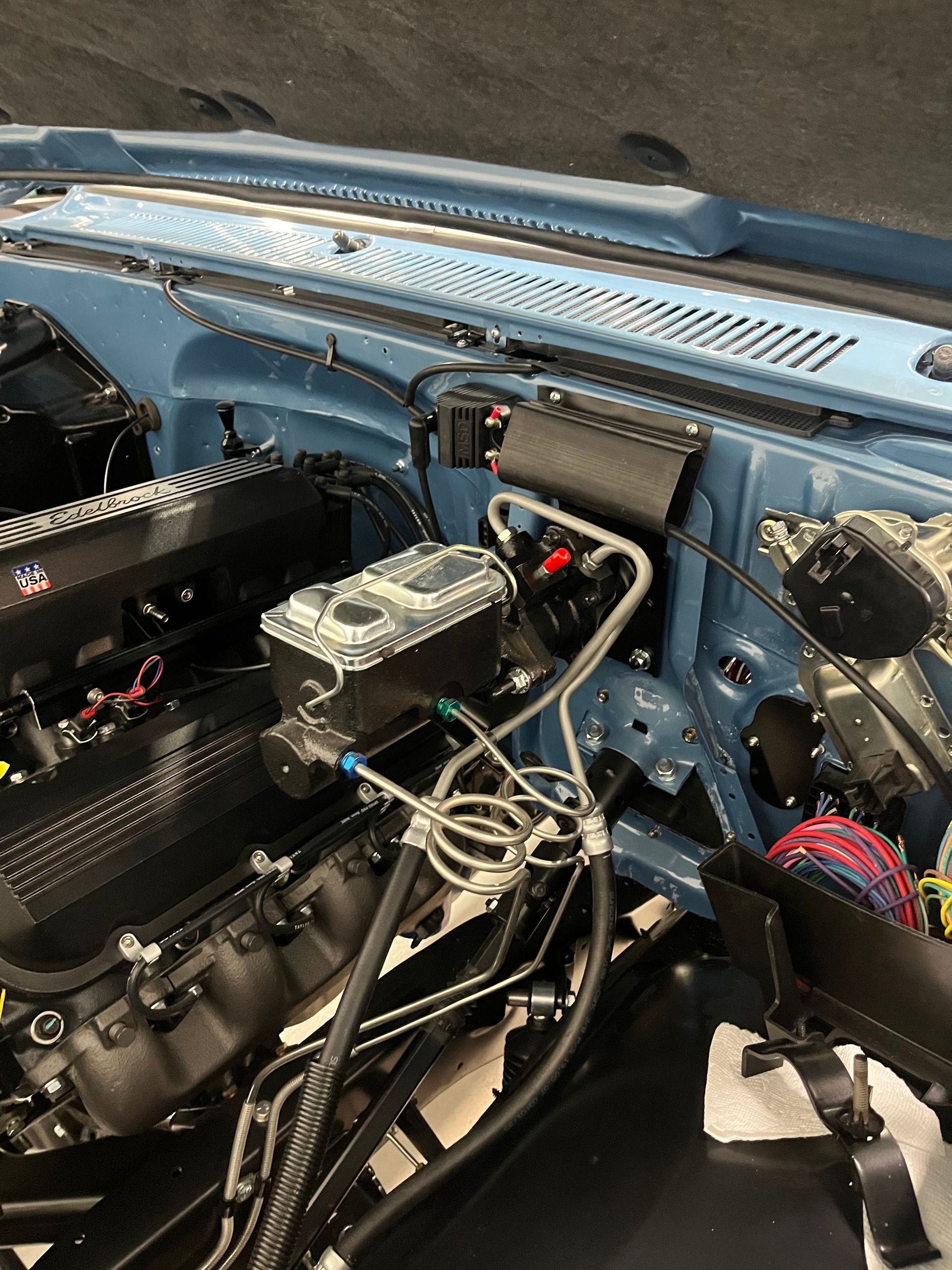 Car engine bay with exposed wiring, hoses, and components inside a blue vehicle frame.