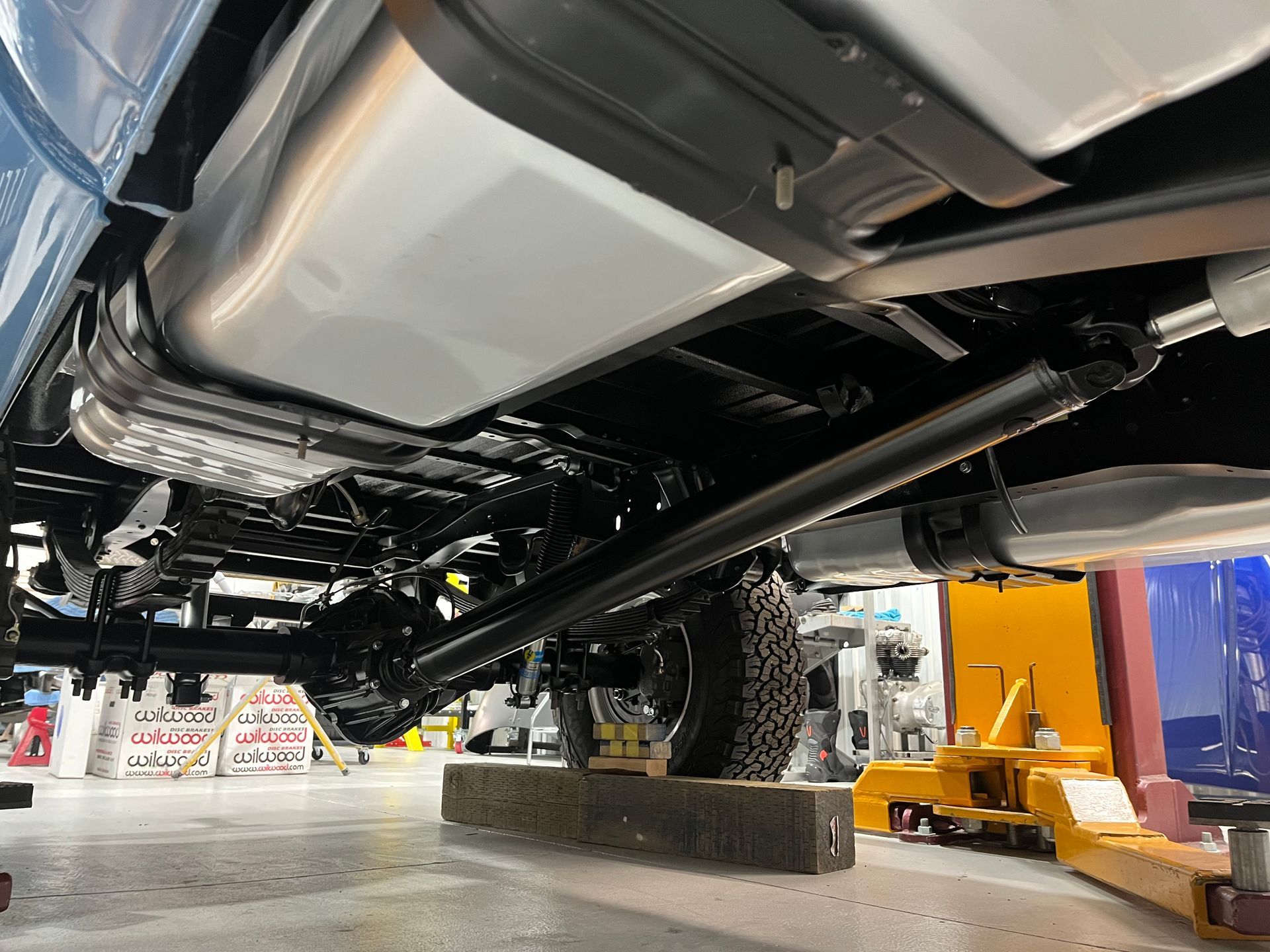 Undercarriage of a car on a lift in an auto repair shop, with a mechanic and tools nearby