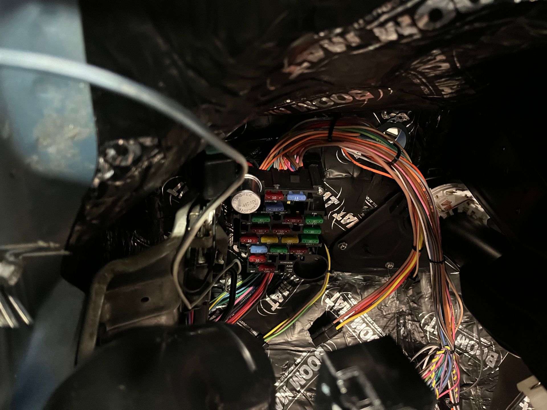 Car fuse box with exposed wiring and colorful cables inside a vehicle dash